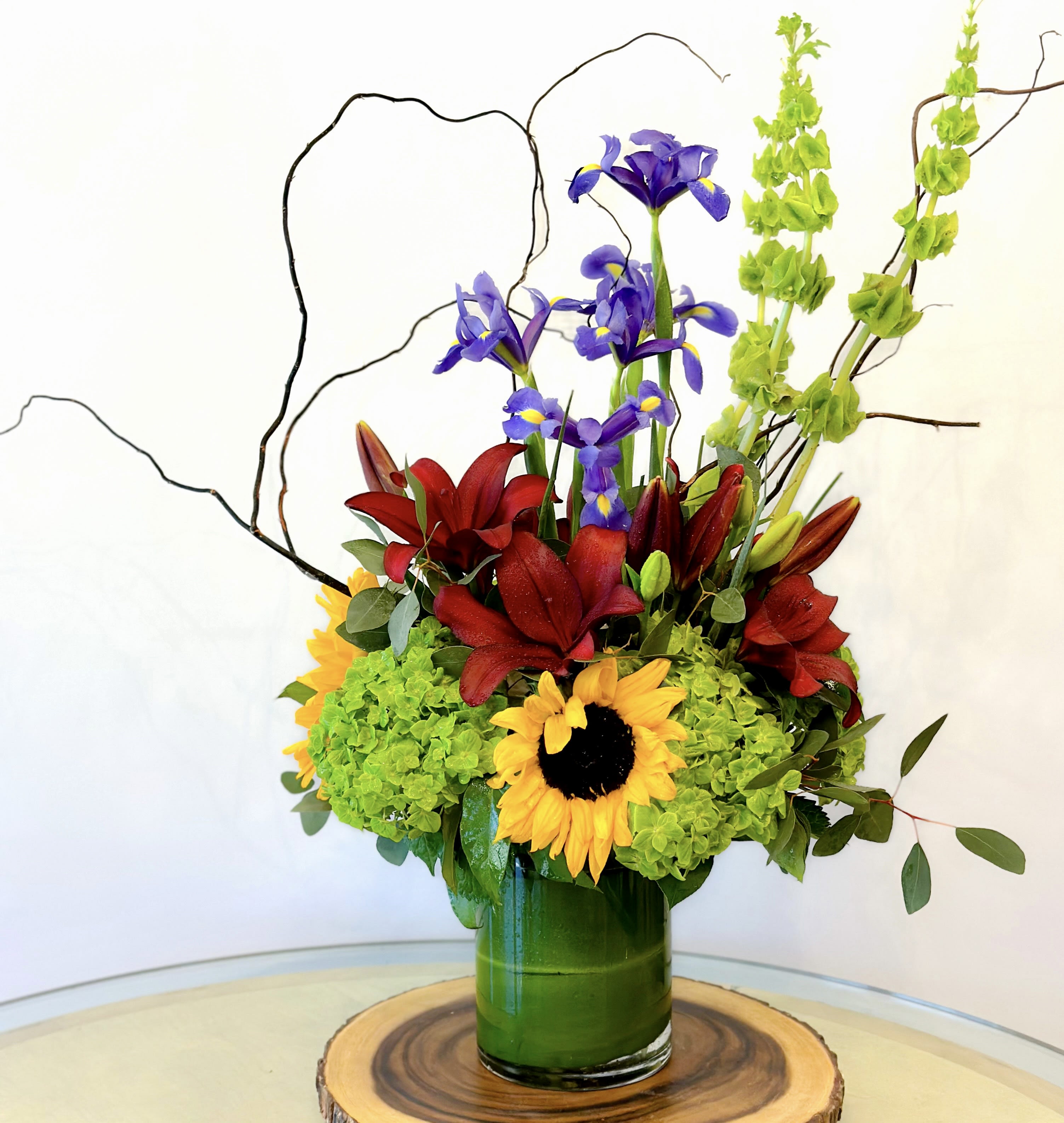 Colorful floral arrangement with sunflowers, red lilies, and purple irises in a green vase