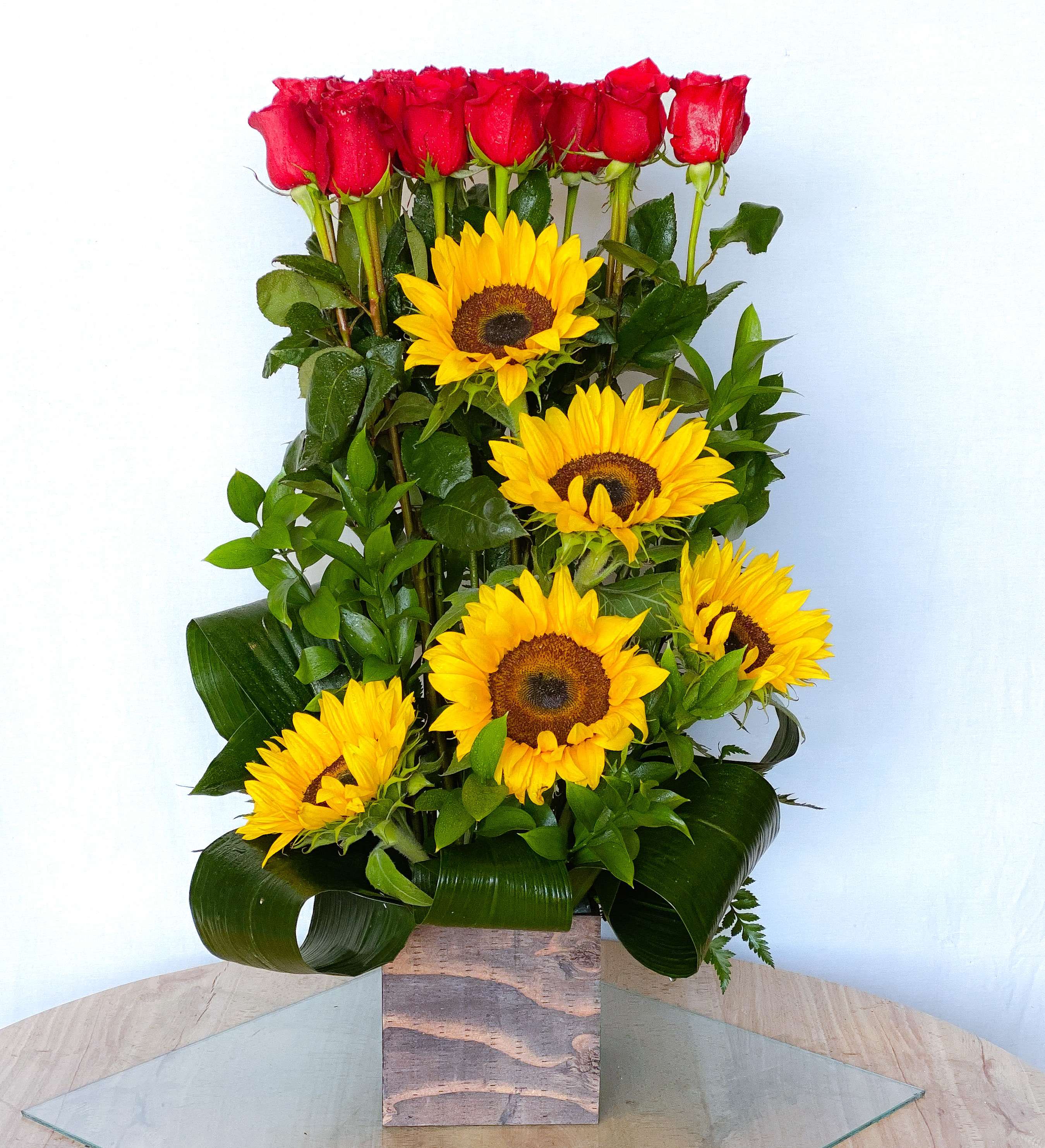 Tall arrangement of red roses and yellow sunflowers in a square vase