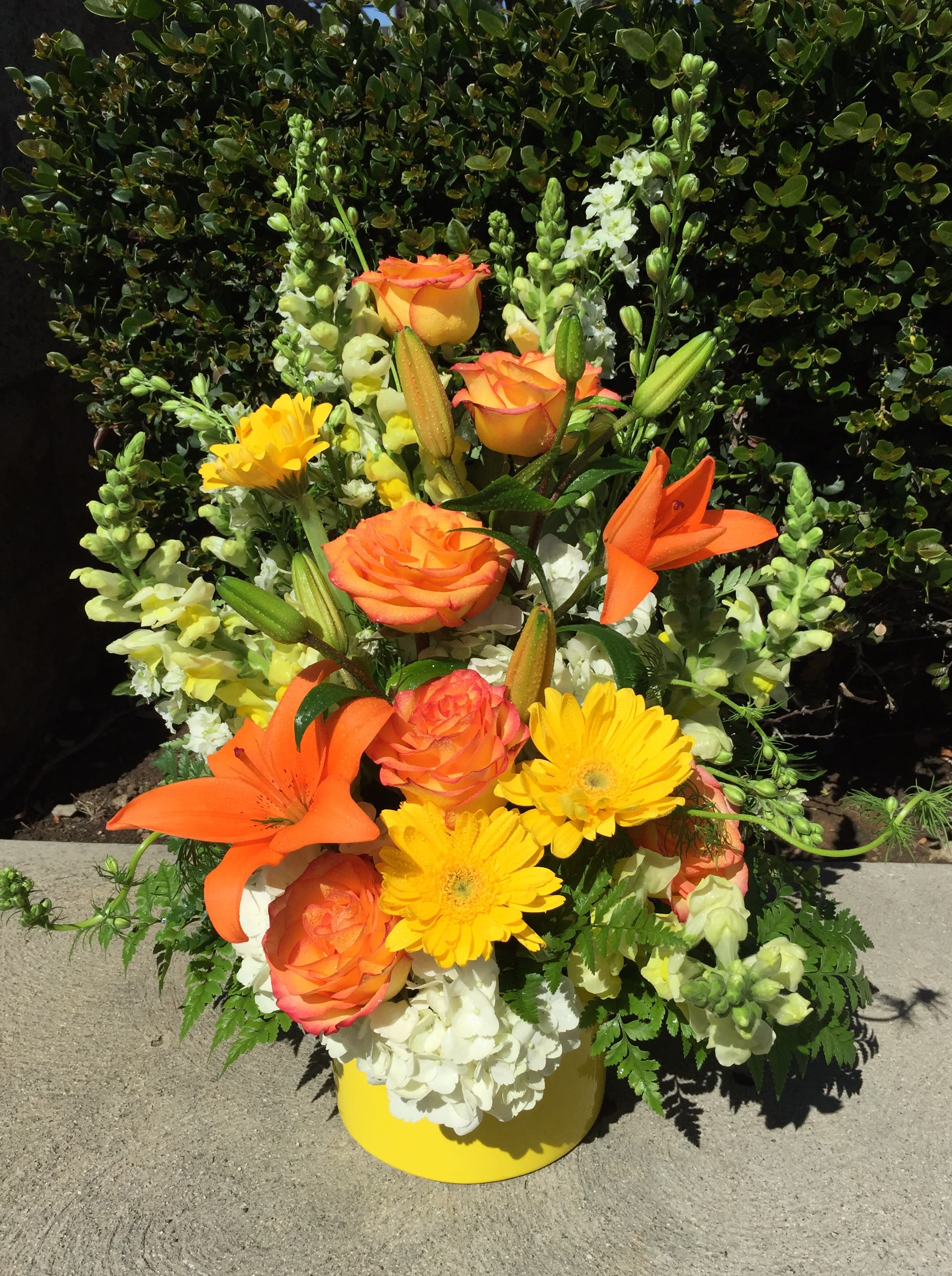 Orange roses and lilies with yellow daisies in a yellow vase