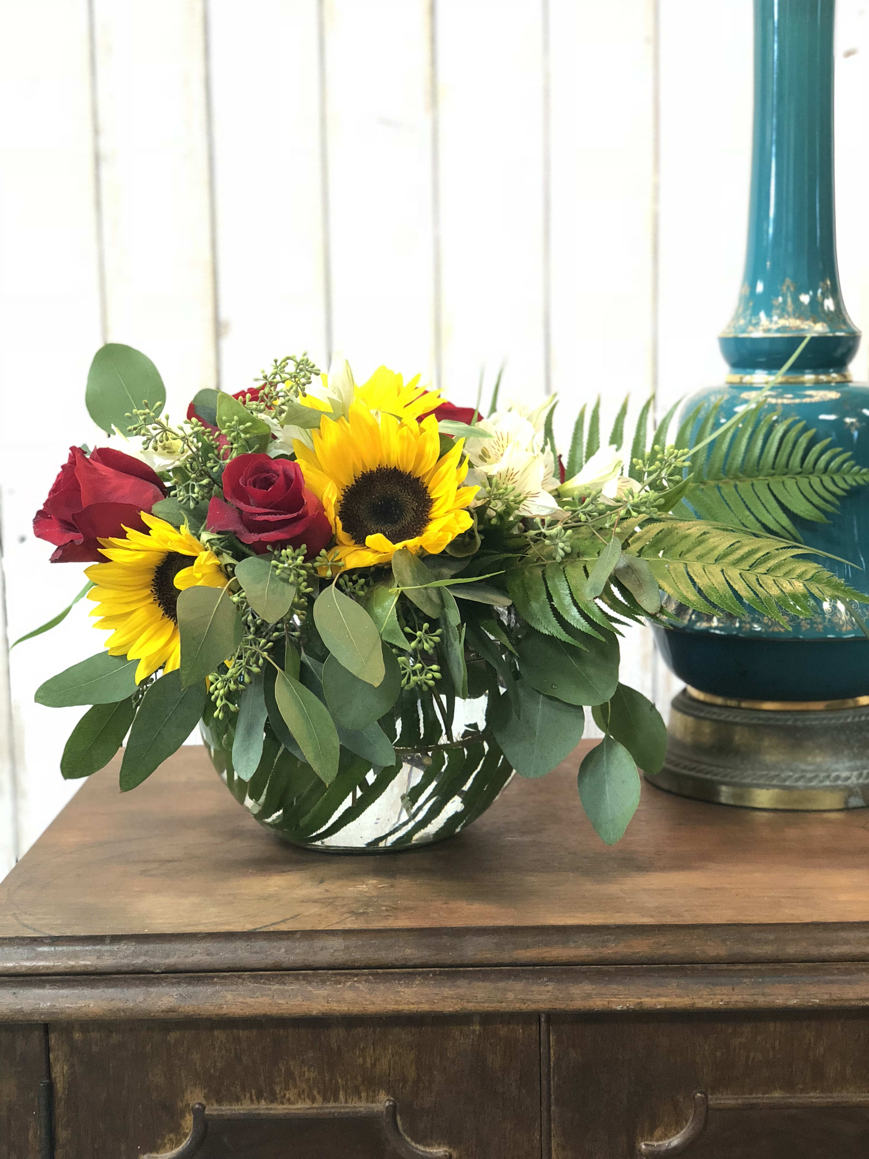 Bouquet of red roses and sunflowers in a low glass vase