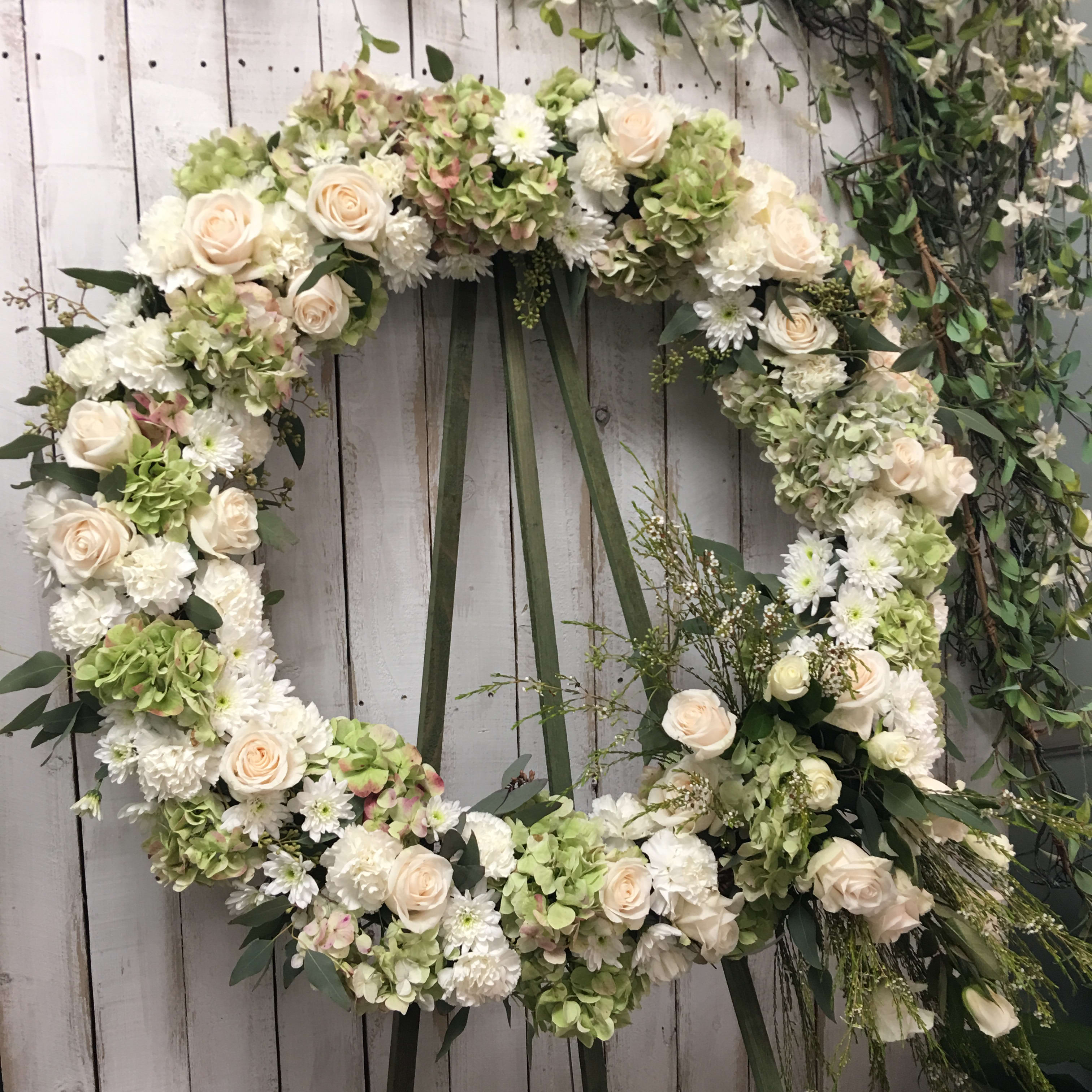 Large floral wreath with white and pale green flowers on a wooden backdrop