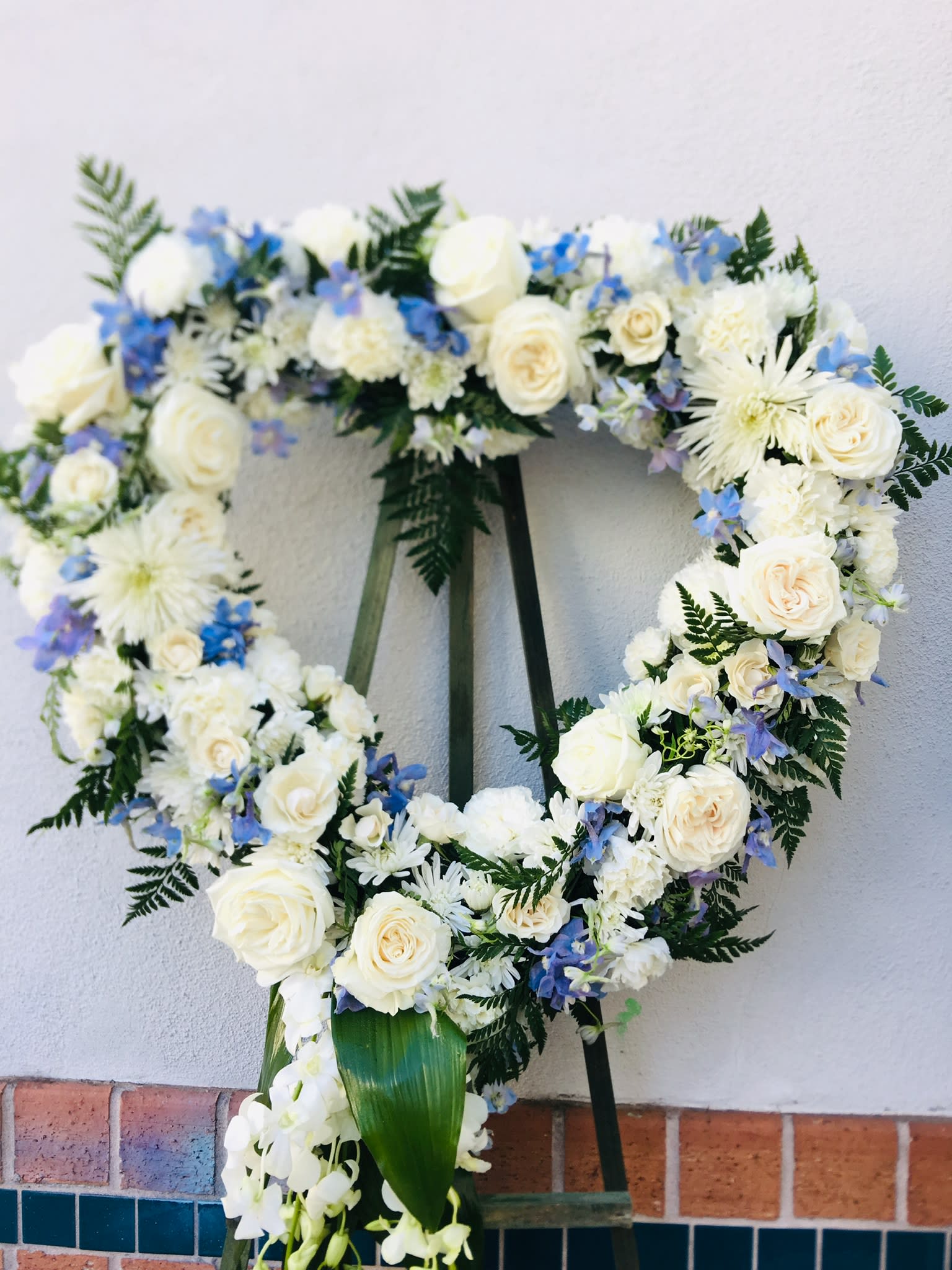 Heart-shaped floral wreath with white roses and blue flowers on an easel