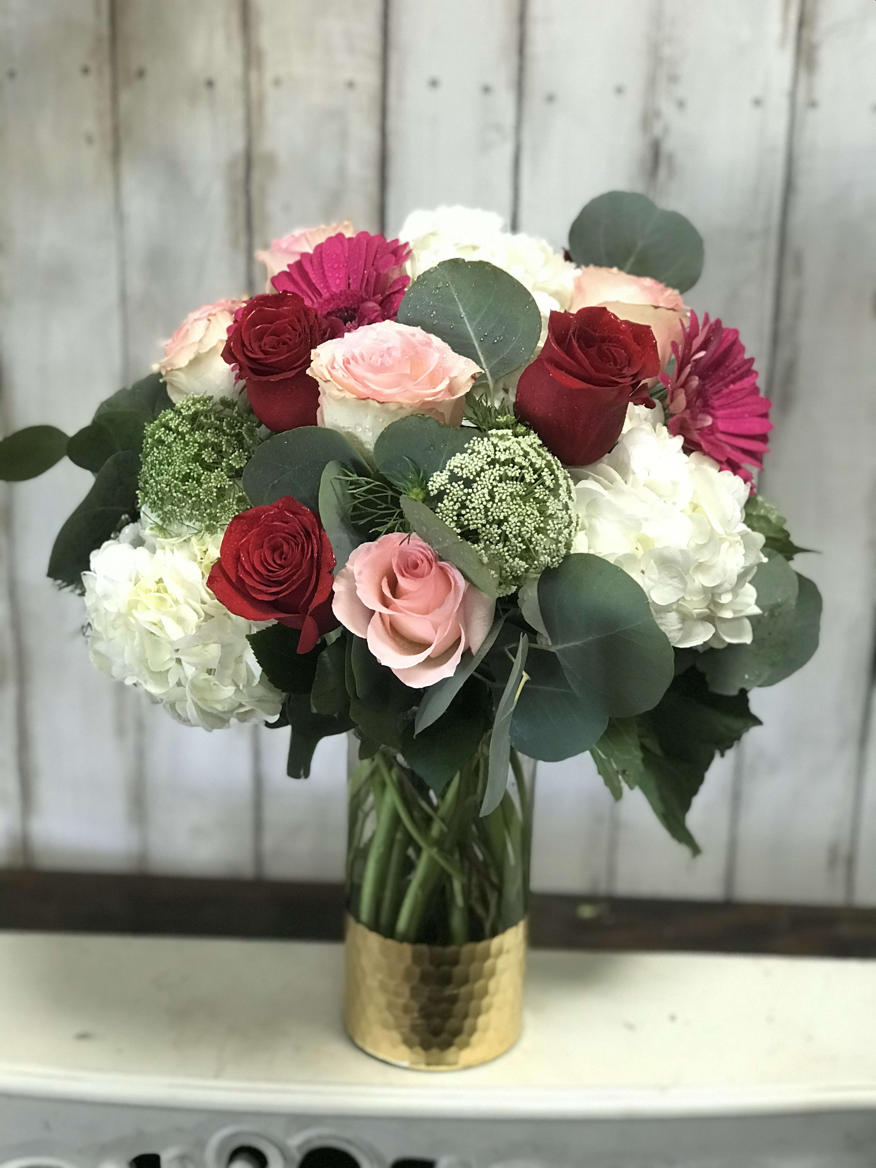Full of Love - This isn’t your typical rose arrangement. This bouquet is arranged with Pink and Red Roses, Hydrangeas, and hot pink Gerbera daisies . It is then accented with eucalyptus greens and finished in our classic gold vase. Perfect for your Valentine  SUBSTITUTION POLICY Always deliver the freshest flowers! Please note the bouquet pictured reflects our original design.  If the exact flowers or container in this arrangement are not available, our local florists will create a beautiful bouquet with the freshest available flowers.