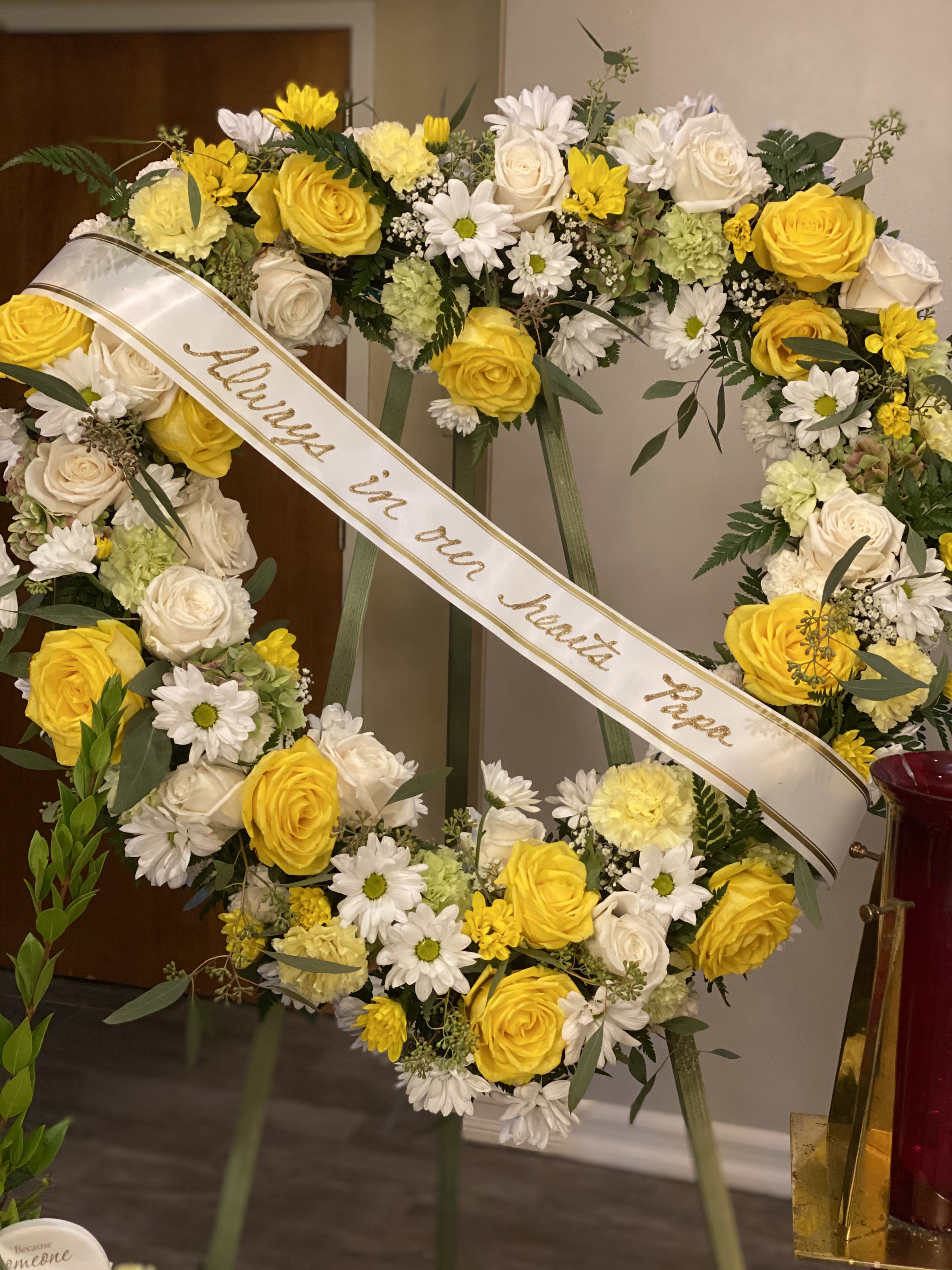 Open Heart  - This heart shaped spray is designed with yellow and white roses, carnations, daisies, and a mixture of foliage.  Ribbon is optional. Message on ribbon is customizable. 