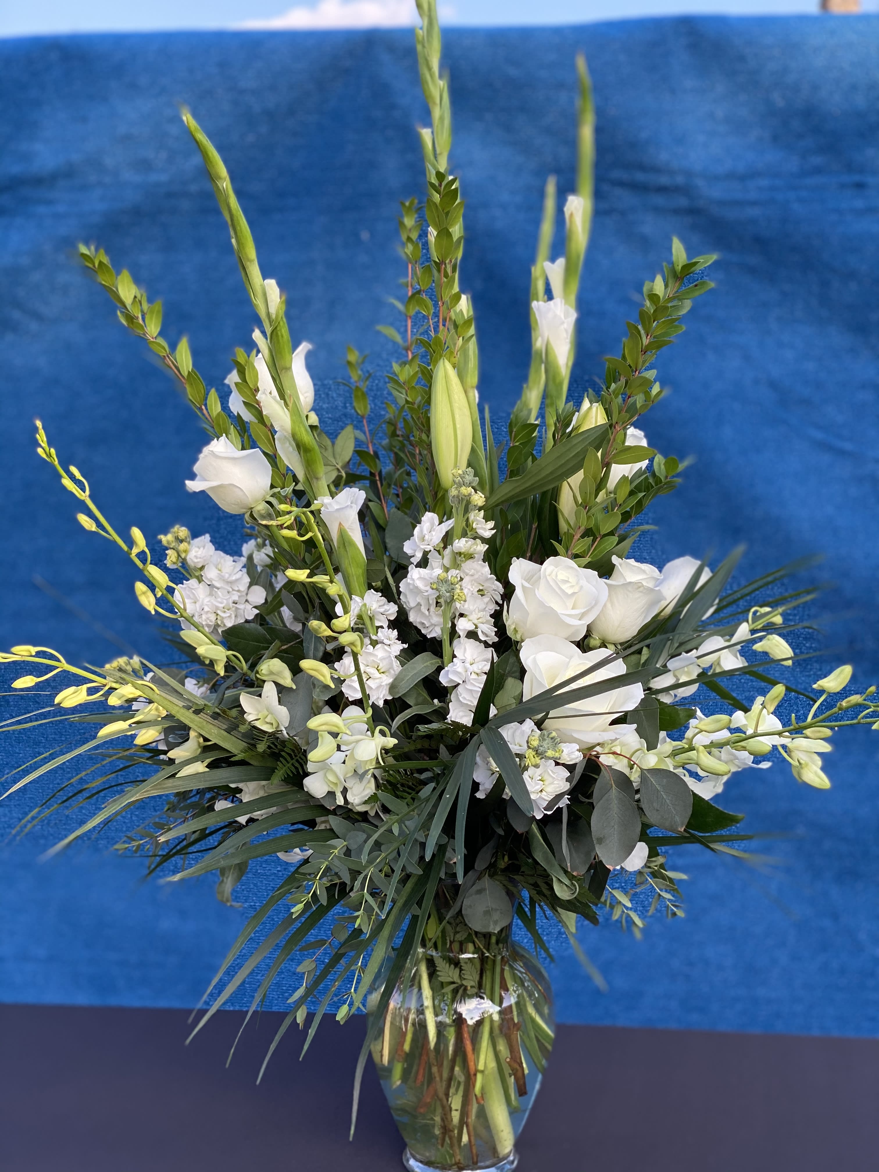Heavenly Heights Bouquet - As peaceful and beautiful as a starry night, this pure white funeral bouquet is a touching way to remember a truly special person. Send this classic arrangement to comfort the newly bereaved at the funeral. Fresh white oriental lilies roses orchids gladiolus and carnations are mixed with rich greens Foliage