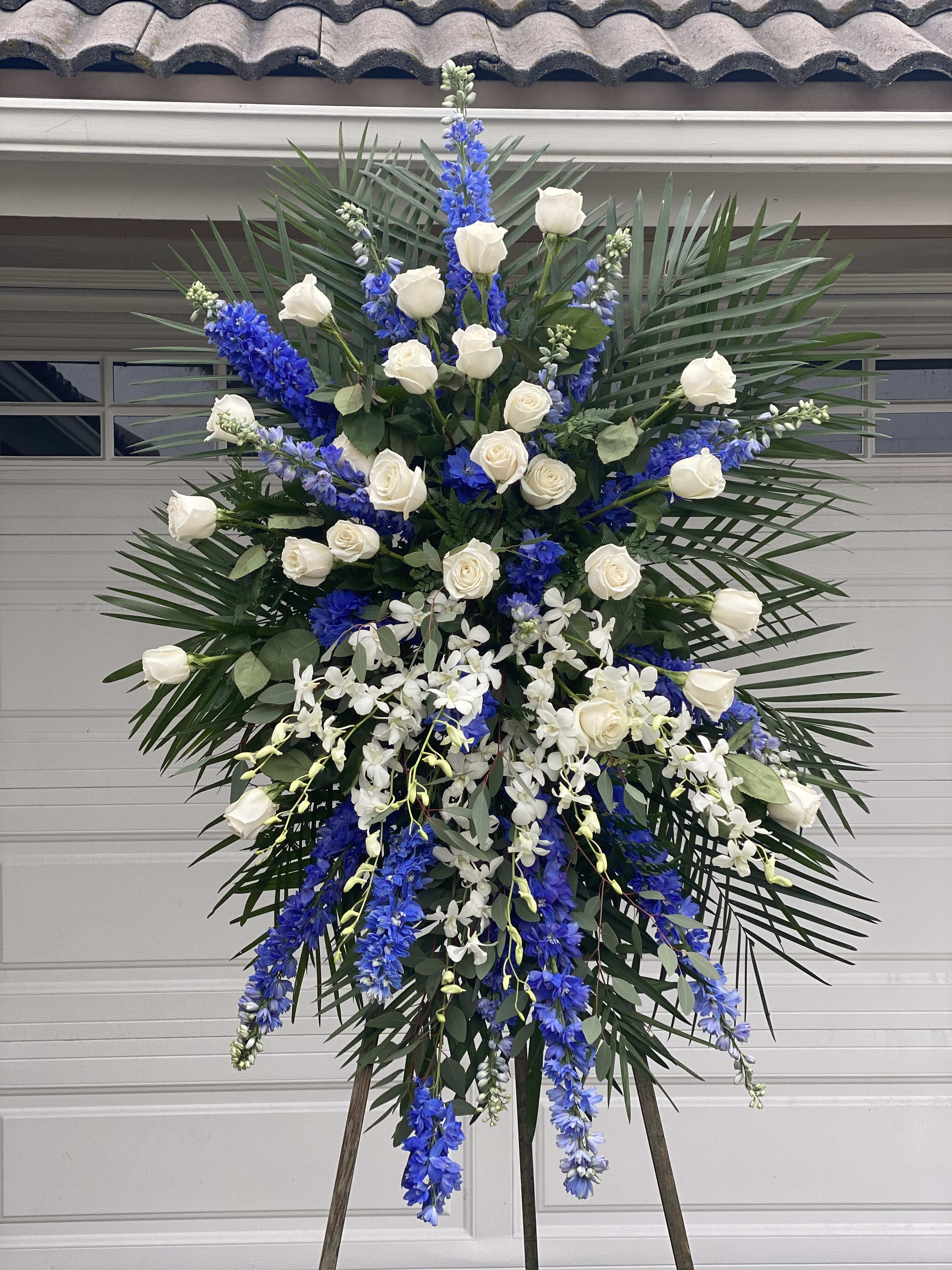 Tall standing floral spray with white roses, blue delphinium, and white orchids