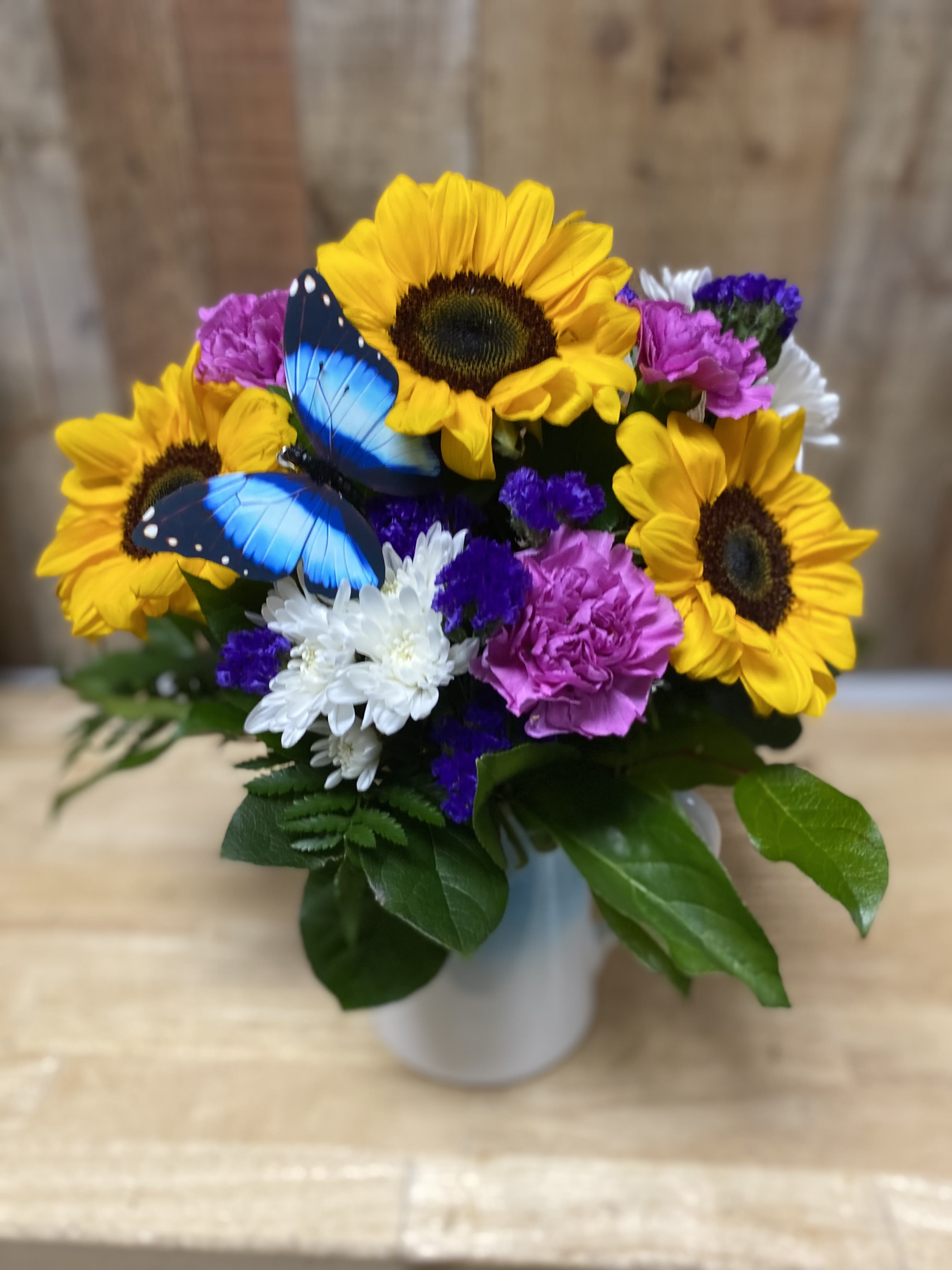 Butterfly Kisses - This a the cutest arrangement designed in a keepsake container pitcher vase with sunflowers carnations filler flowers 