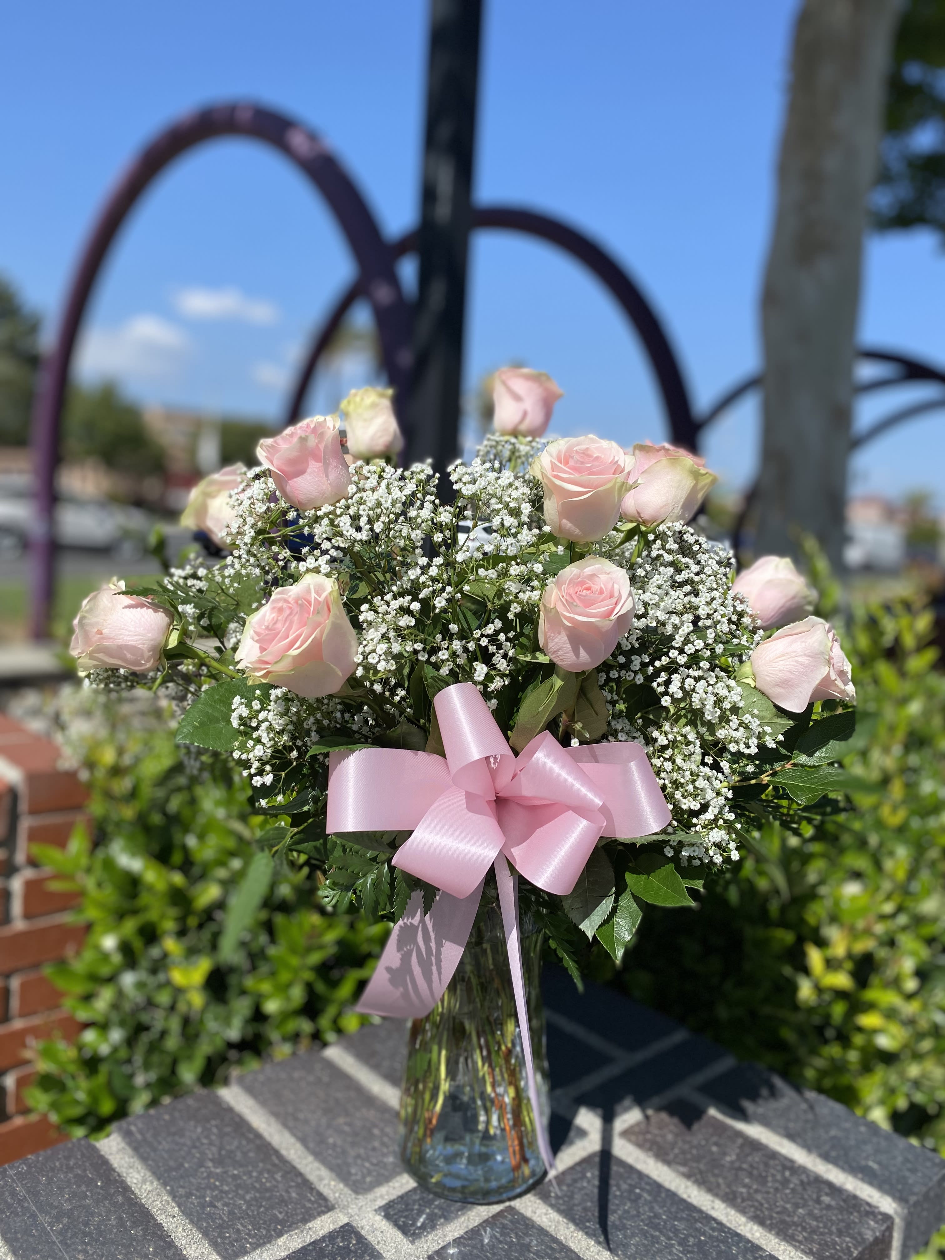 Pink roses and baby's breath in a clear glass vase with a pink ribbon