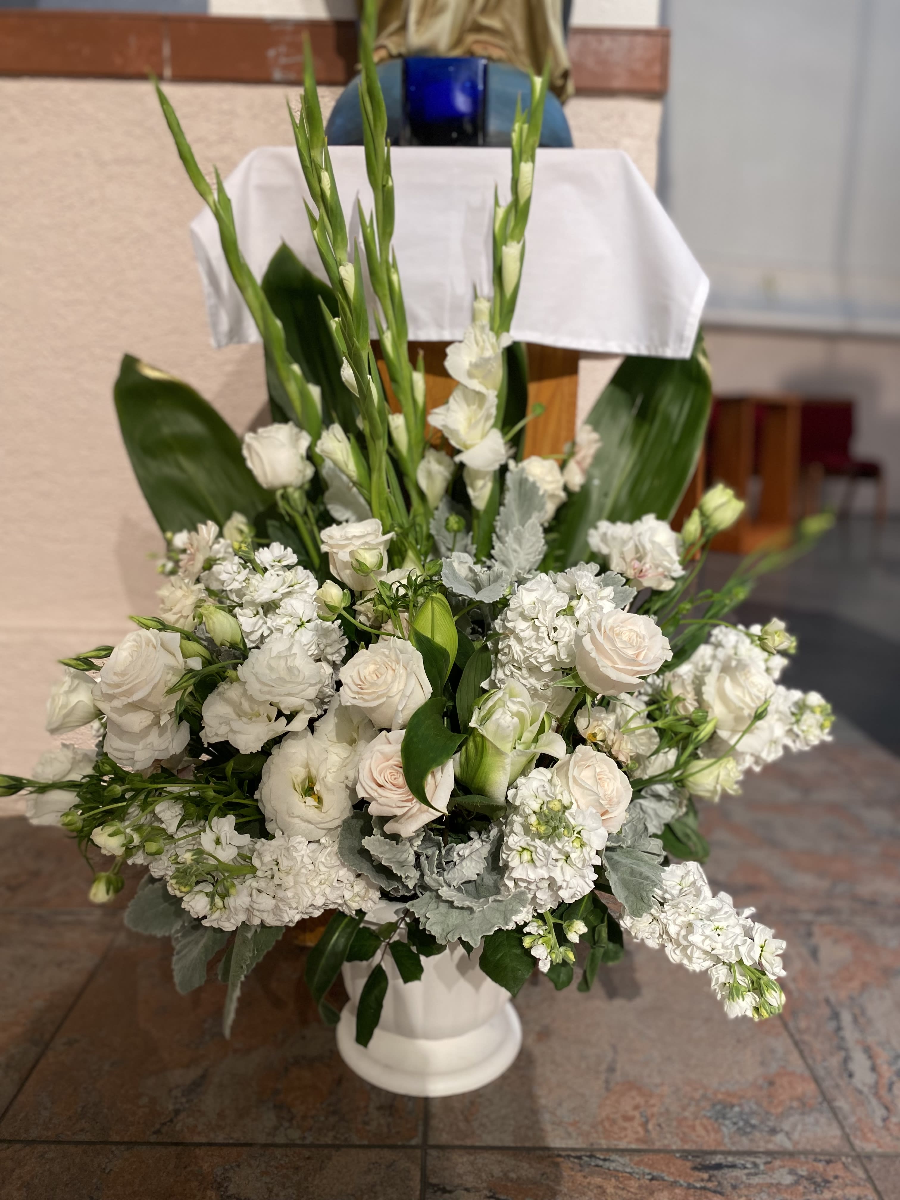 White floral arrangement in a white pedestal vase with tall green stems