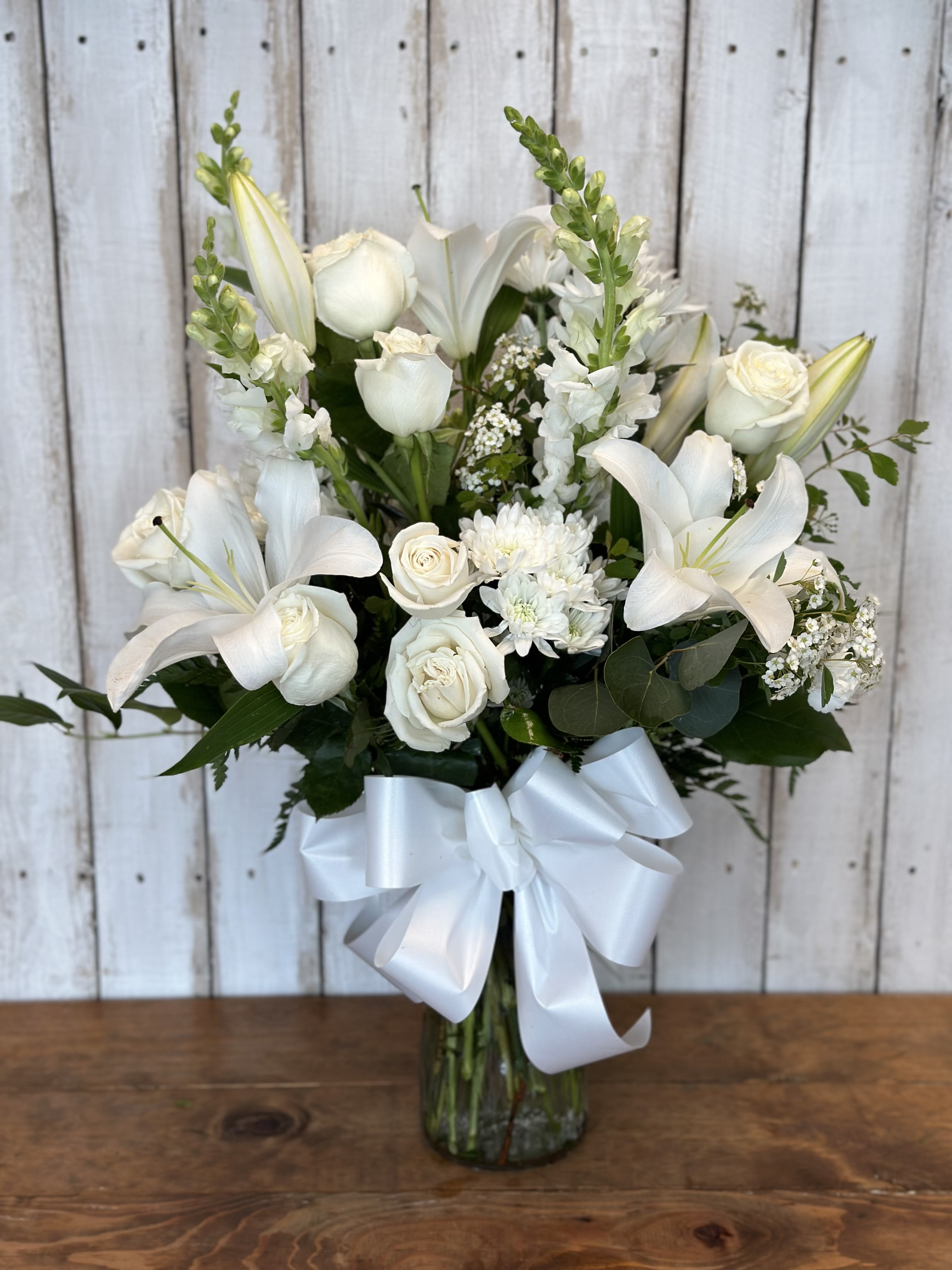 White lilies and roses arranged in a glass vase with a white ribbon