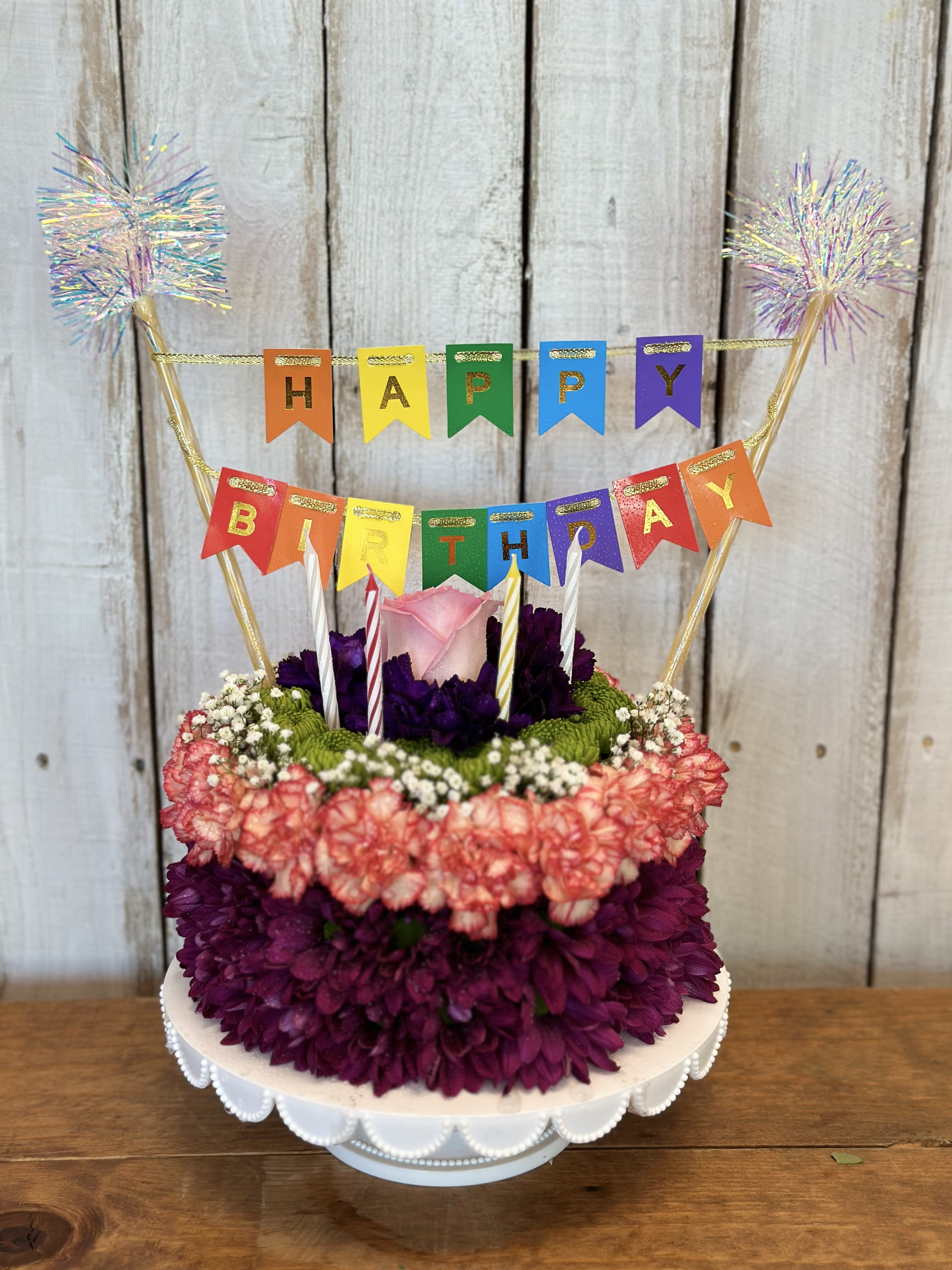Birthday cake decorated with flowers and a colorful HAPPY BIRTHDAY banner