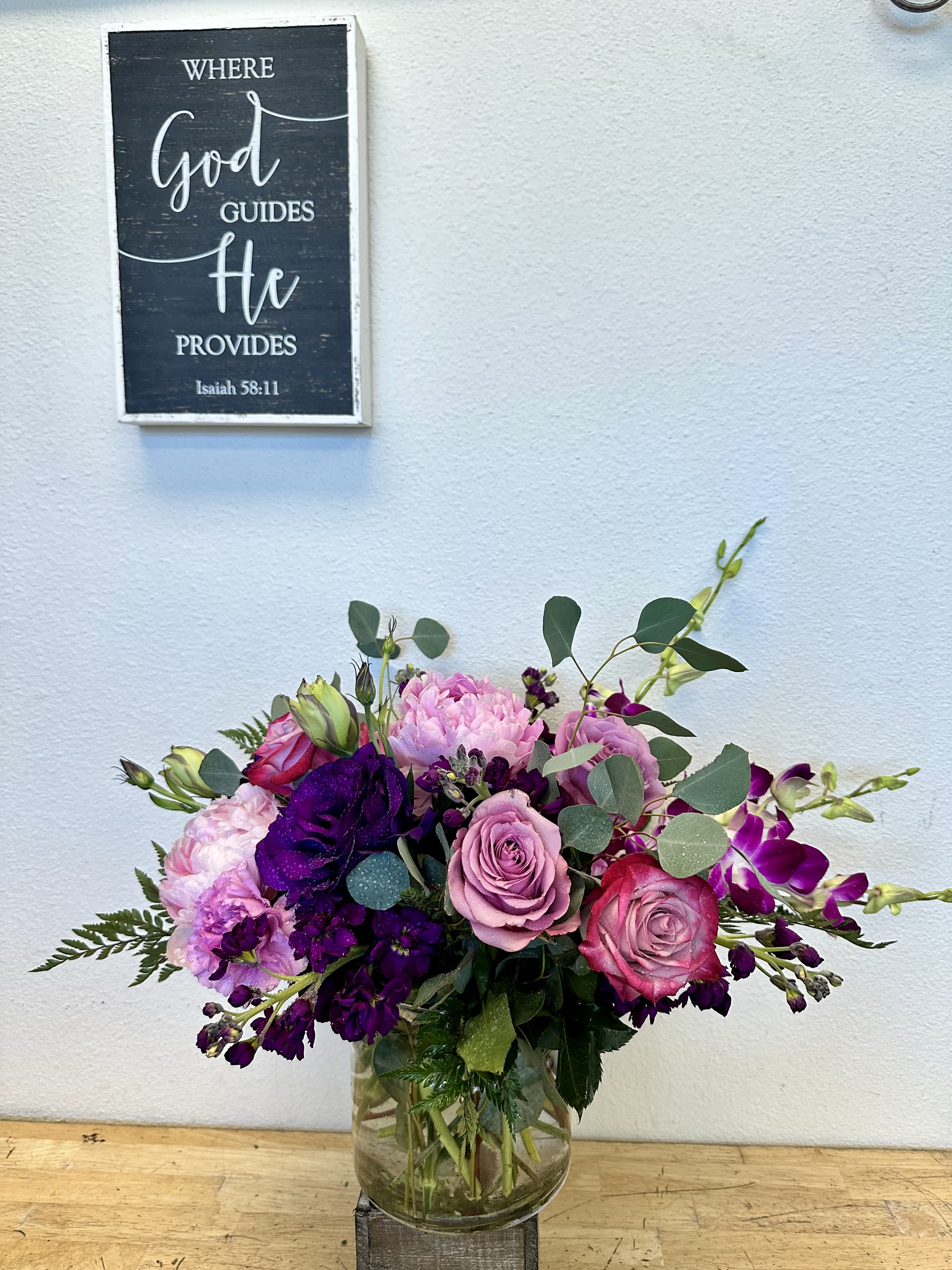 Lavender bliss - Delight in the beauty of soft elegance with this stunning compact arrangement. Featuring Dendrobium orchids, lavender roses, peonies, carnations, and purple Lisianthus, all nestled among lush seeded eucalyptus and silver dollar Eucalyptus foliage, this design showcases shades of lavender, purple, and pink. Perfect for adding charm to any occasion!  This arrangement highlights the lavender and purple tones beautifully.  Please note that substitutions may be made based on seasonal availability. Contact us for more details and customization 