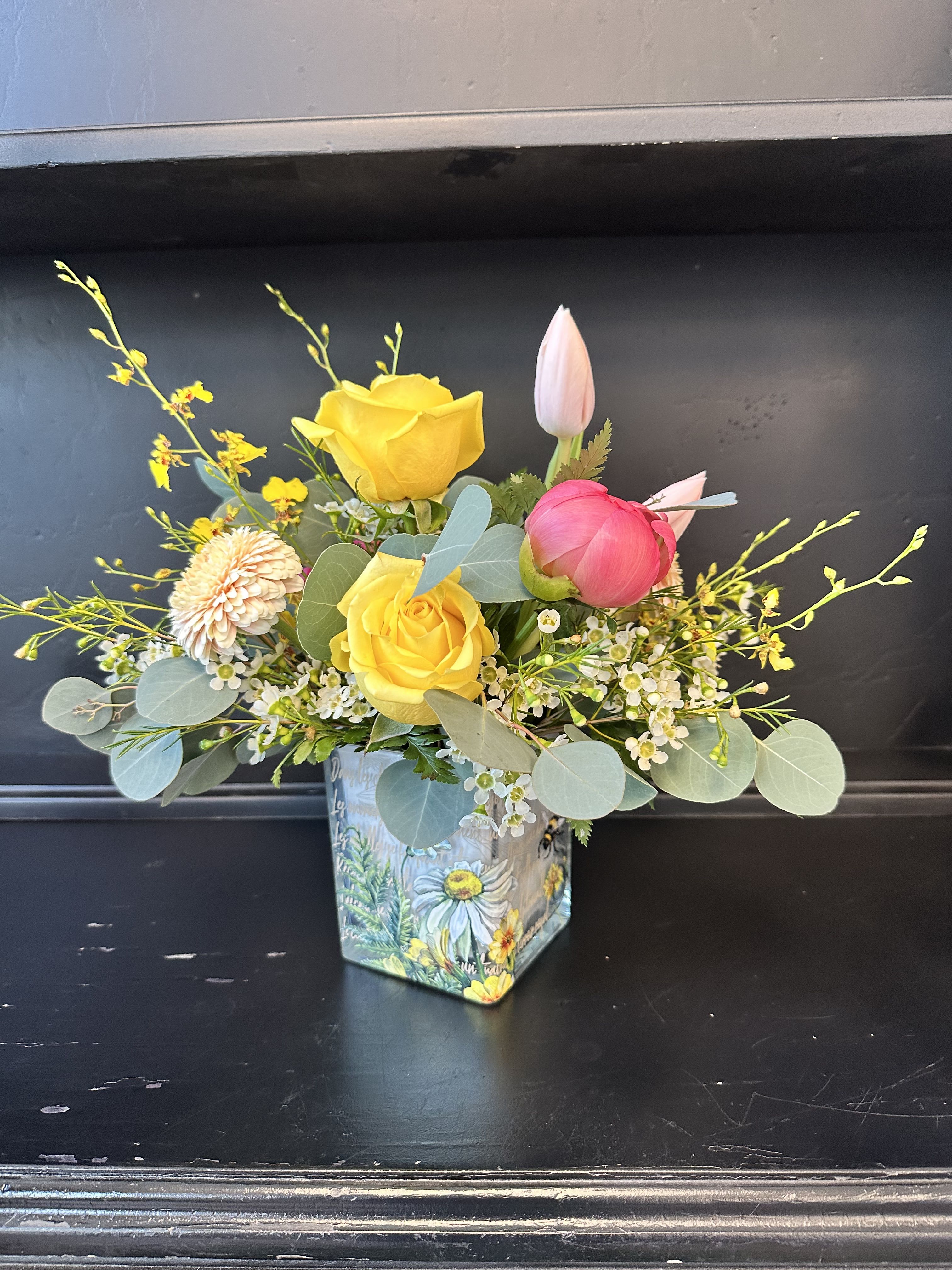 Bee-utiful Blossoms - Bee-utiful Blossoms A Delightful Floral Arrangement Brighten someone’s day with this charming and whimsical arrangement, overflowing with elegance and joy! Featuring lush peonies, delicate ranunculus, vibrant tulips, and exquisite Oncidium orchids, this stunning bouquet is artfully designed in a glass cube vase adorned with hand-painted daisies and buzzing bumblebees.