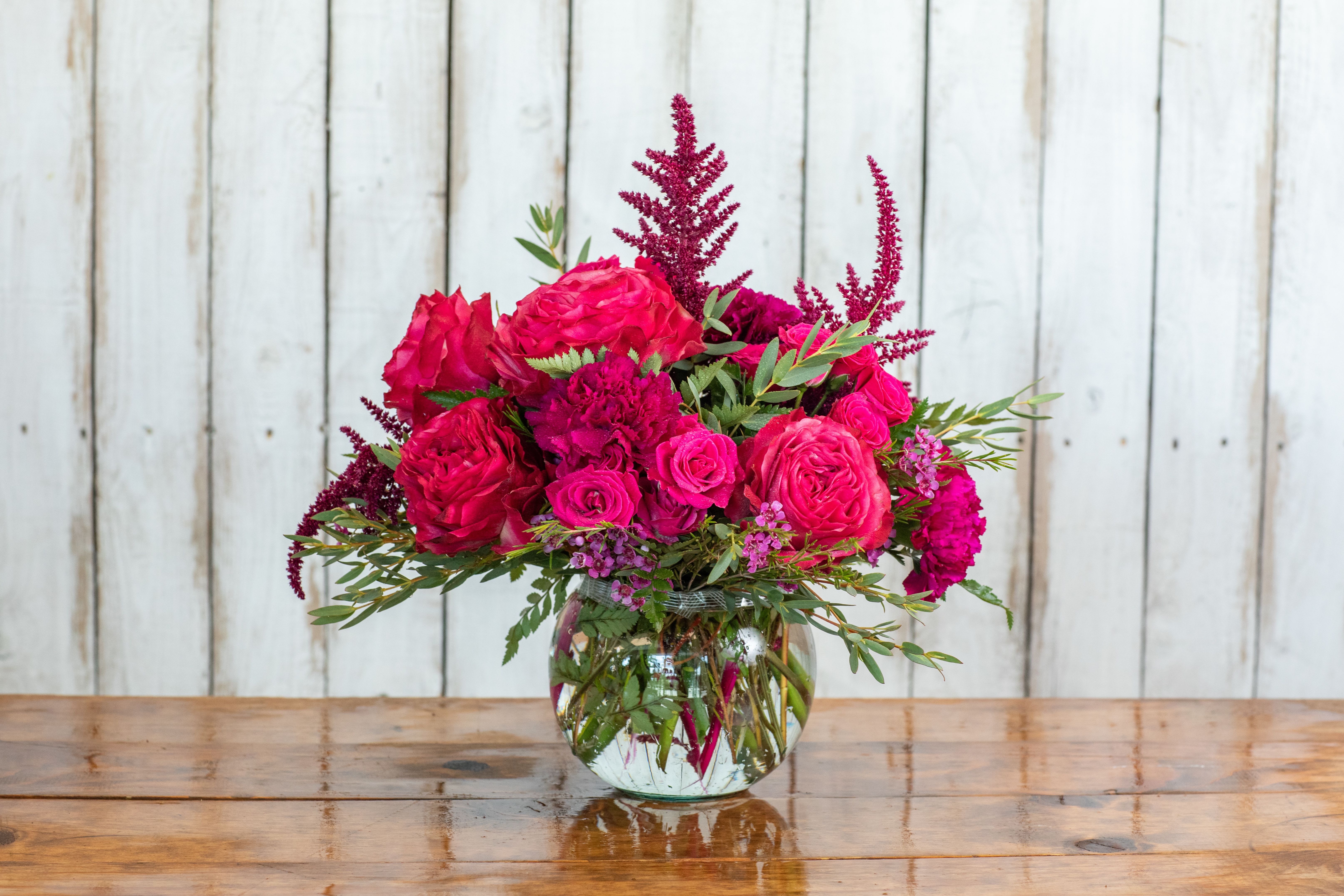 Rancho Rhapsody Bouquet - Experience the vibrant beauty of our Rancho Rhapsody Bouquet, a stunning arrangement handcrafted by your local Rancho Cucamonga Florist, Tommy Austin Florist.  This breathtaking centerpiece overflows with rich, jewel-toned blooms in shades of fuchsia, deep magenta, and crimson. It features luxurious garden roses and spray roses nestled amongst delicate carnations and the feathery texture of astilbe. Lush eucalyptus greenery provides a beautiful, aromatic contrast. Presented in a classic glass vase, the "Rancho Rhapsody" is the perfect way to make a bold, romantic statement for a special anniversary, a celebratory birthday, or simply to brighten someone's day with an unforgettable splash of color. Hand-delivered fresh from our shop to homes and businesses across Rancho Cucamonga and beyond.