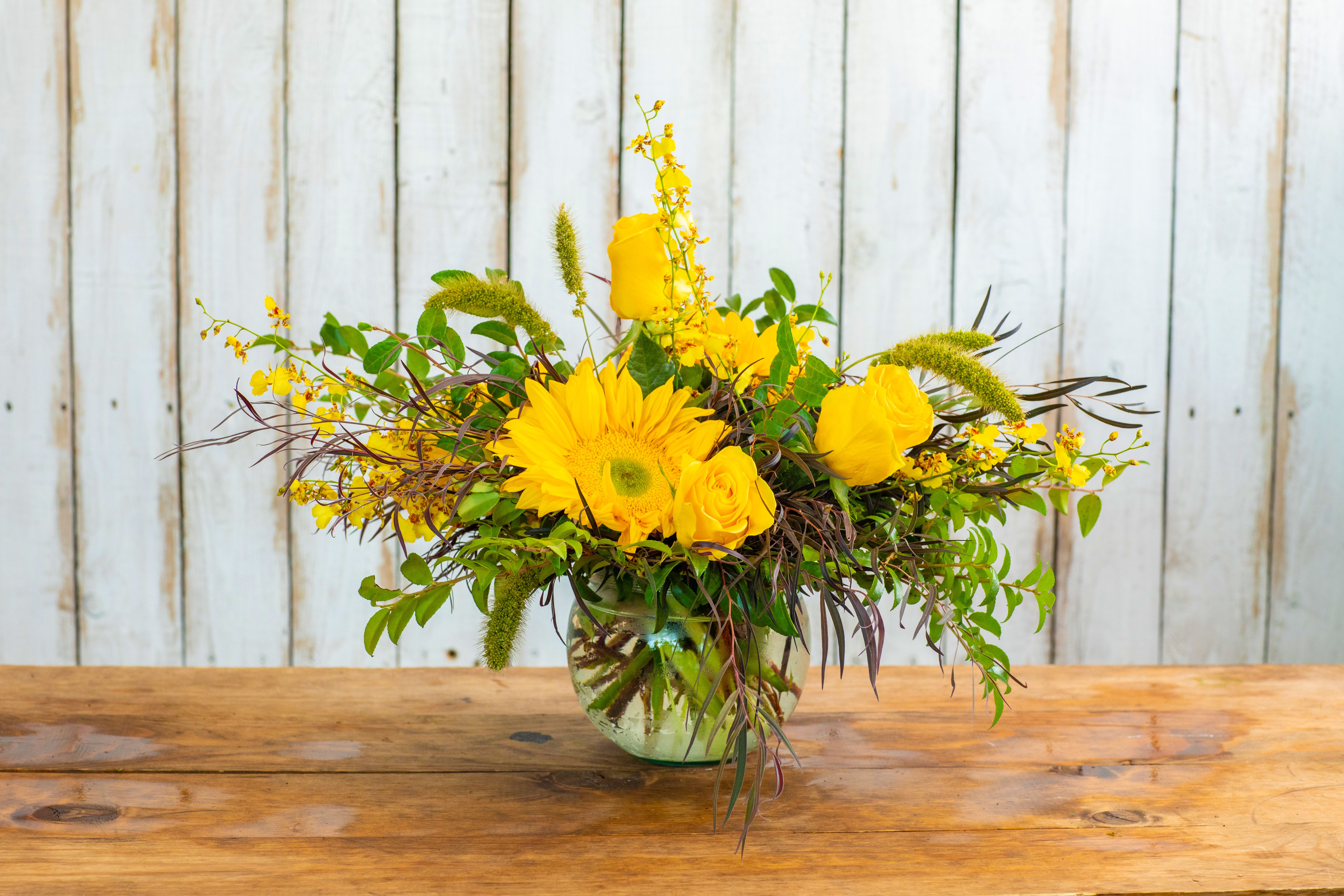 Sunny Meadow Delight - Brighten any day with the Sunny Meadow Delight, a cheerful and vibrant arrangement expertly crafted by your local Rancho Cucamonga Florist. This radiant bouquet is a burst of sunshine, featuring a playful mix of bright yellow blooms.  It showcases a charming sunflower as its centerpiece, surrounded by elegant yellow roses and delicate yellow spray orchids. Unique green wheat-like accents and varied lush greenery add wonderful texture, all artfully arranged in a contemporary clear glass bowl. It’s the perfect flower gift to send!  As the leading Rancho Cucamonga flower shop, we make it easy to shop for flowers that spread happiness. This sunny arrangement is an ideal choice for a joyful birthday bouquet, a thoughtful get well soon gift, a cheerful thank you gesture, or simply to bring a smile to someone’s face.  We offer reliable same-day flower delivery throughout the entire Rancho Cucamonga area. Don't wait—order flowers now and trust our expertise to deliver a stunning and uplifting arrangement. Buy the Sunny Meadow Delight online today from your dependable local Rancho Cucamonga Florist!