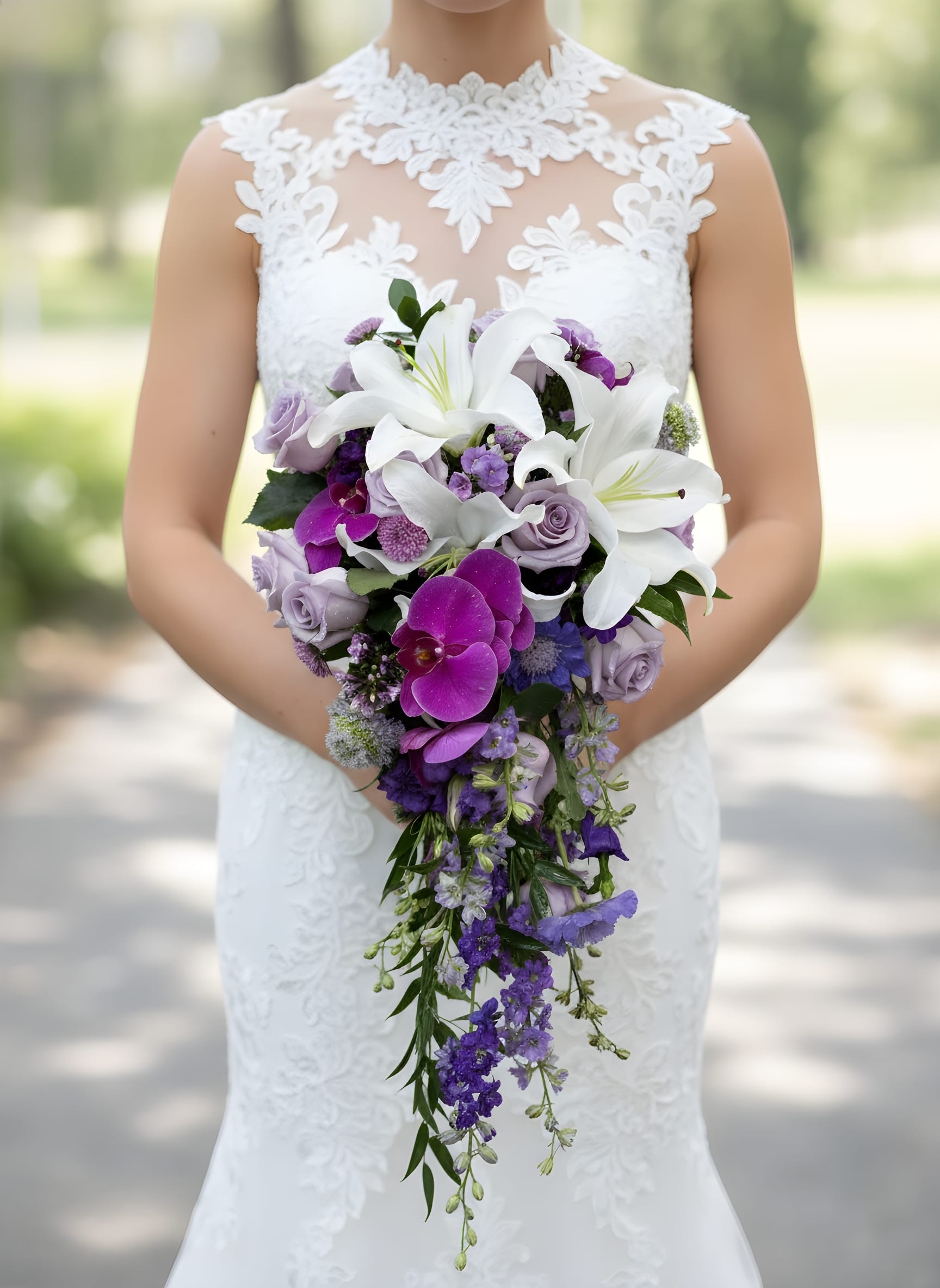 Lavender Orchid Cascade Bridal Bouquet - Make a breathtaking entrance with our Lavender Orchid Cascade Bridal Bouquet, a luxurious wedding bouquet designed for the romantic bride. This elegant cascading arrangement features premium white oriental lilies, lavender roses, vibrant purple orchids, delphinium, and seasonal garden blooms accented with flowing greenery.  The soft lavender and rich purple tones symbolize love, grace, and enchantment, while the cascading design creates a timeless, sophisticated look perfect for vineyard weddings, garden ceremonies, church weddings, and upscale celebrations.  Handcrafted by Tommy Austin Florist, each bouquet is created with premium flowers and artistic attention to detail, ensuring a stunning statement piece for your walk down the aisle.  Features:  * Premium white oriental lilies * Lavender roses * Purple orchids * Delphinium and seasonal accent flowers * Elegant cascading design * Handcrafted with fresh premium blooms * Ideal for romantic, garden, vineyard, and luxury weddings