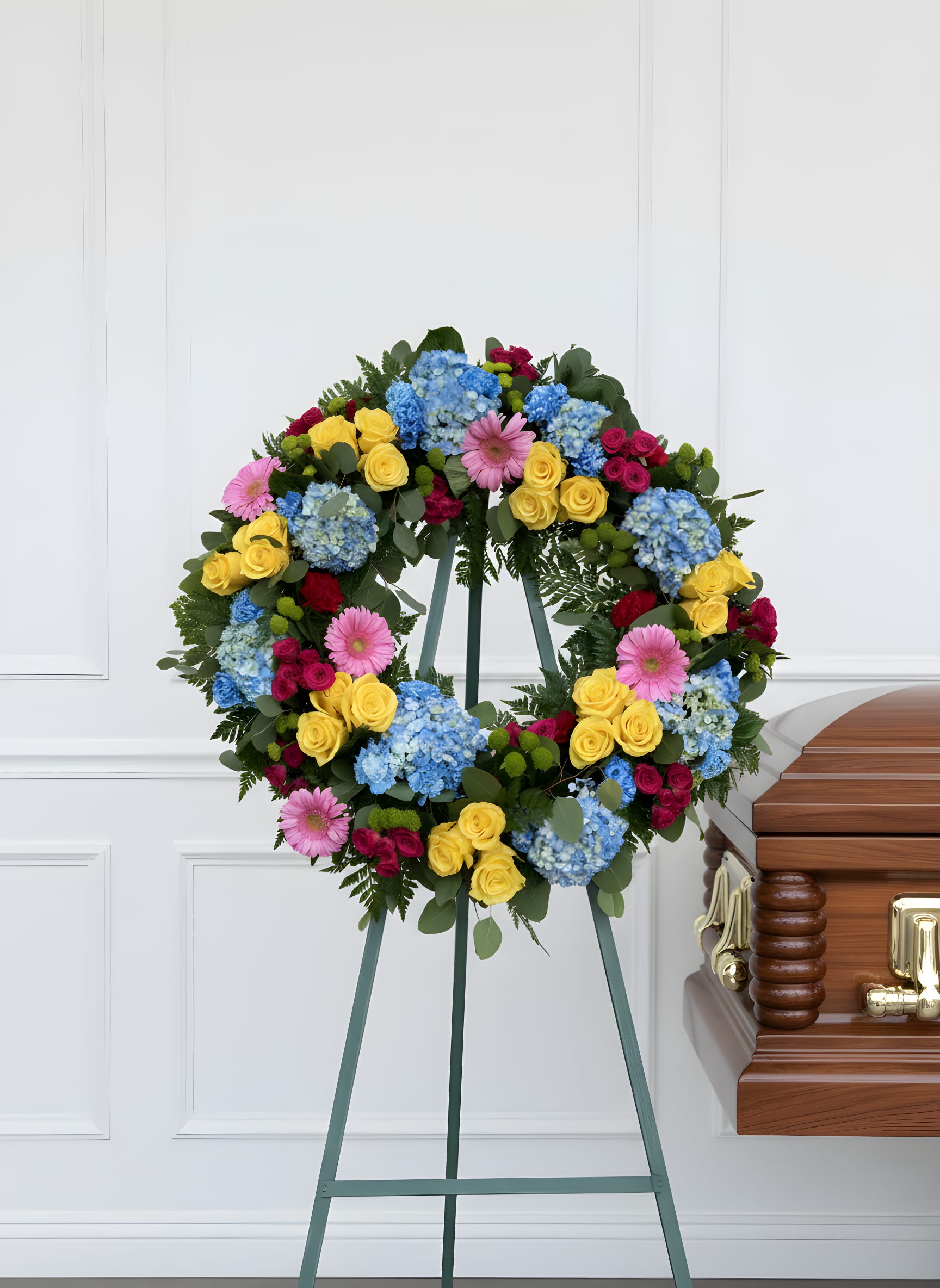 Sunshine &amp; Sky Tribute Wreath - Honor a beautiful life with our Sunshine &amp; Sky Tribute Wreath, a vibrant standing spray designed to celebrate cherished memories and a life well lived. This colorful sympathy wreath features premium blue hydrangeas, sunny yellow roses, pink gerbera daisies, vibrant spray roses, green button poms, and lush seasonal greenery arranged in a classic circular design symbolizing eternal love and remembrance. Handcrafted by Tommy Austin Florist, this elegant funeral wreath offers comfort, hope, and heartfelt condolences during life’s most difficult moments. Perfect for funeral services, memorial celebrations, celebration of life ceremonies, and graveside tributes. We are able to change colors.  Features:Premium Blue Hydrangeas, Yellow Roses, Pink Gerbera Daisies, Hot Pink Spray Roses, Green Button Poms, Fresh Seasonal Greenery Displayed on an Easel Stand included  Perfect For: Funeral Services • Memorial Services • Celebration of Life Ceremonies • Sympathy Tributes • Graveside Services Local Delivery Available Serving Rancho Cucamonga, Ontario, Upland, Fontana, Claremont, Eastvale, and surrounding Inland Empire communities.