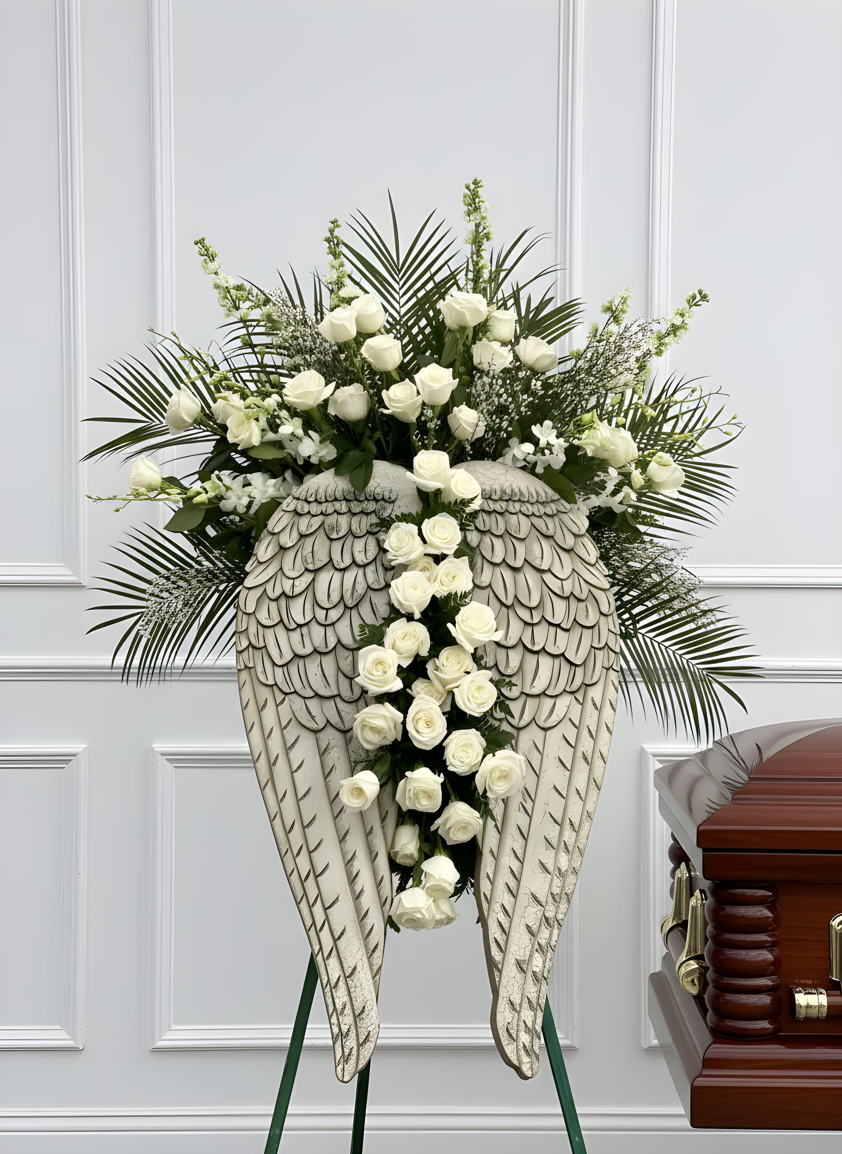 Heaven’s Wings™ Angel Tribute - A breathtaking sympathy tribute designed to honor a beautiful life with peace, grace, and heavenly love. Heaven’s Wings™ Angel Tribute features elegant angel wings surrounded by premium white roses, white orchids, snapdragons, baby’s breath, lush palm leaves, and fresh seasonal greenery. The cascading white roses down the center create a powerful expression of eternal love, remembrance, and faith.  This luxury standing funeral arrangement is perfect for families who want something meaningful, elegant, and unforgettable for a funeral service, memorial, celebration of life, church service, or graveside tribute. Keepsake, angel wings. Wall hangers 