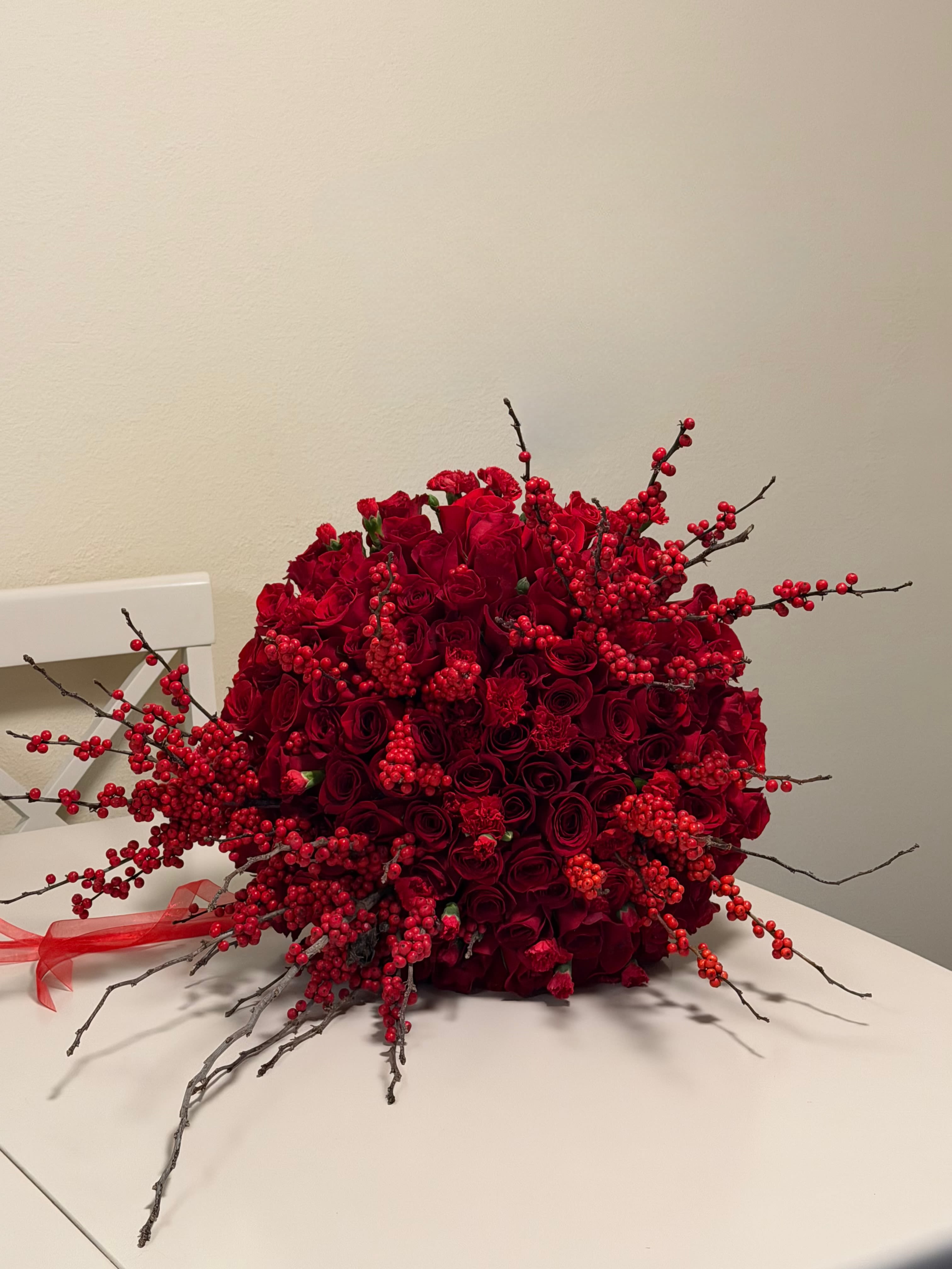 Scarlet impact - This striking arrangement features an abundant display of premium red roses, carnations that meticulously design to create a bold and unforgettable statement. Accented with vibrant red berry branches and natural textured twigs, the composition offers depth, movement, and refined elegance. The rich crimson tones symbolize passion, devotion, and timeless romance, making this arrangement a perfect choice for grand gestures!!