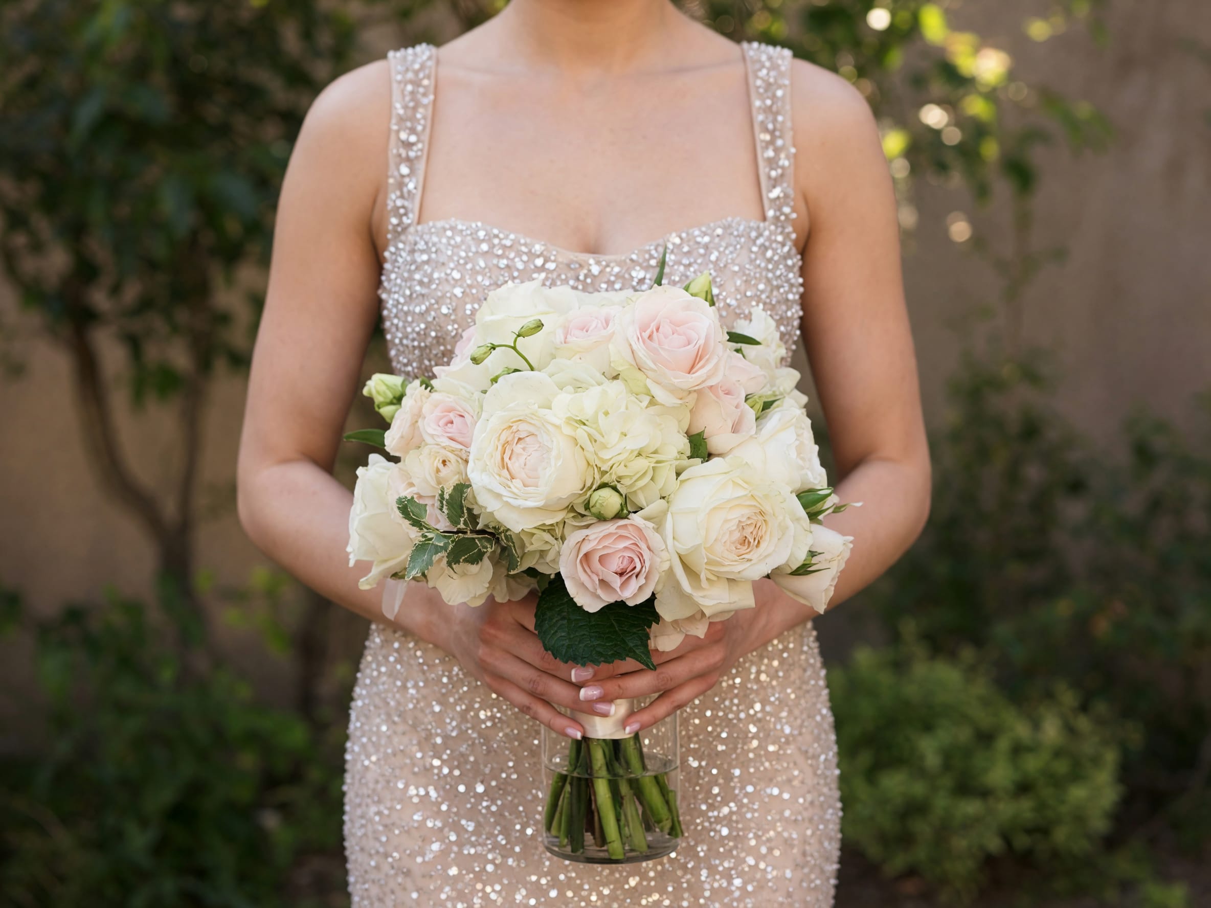 Blush Bouquet  - Creamy white and soft blush roses mingle with pale hydrangea blooms to create a romantic flower arrangement perfect for a wedding bouquet or anniversary gift. The Blush Bouquet reads as elegant and classic-an intimate, hand-held style that makes the person you're thinking of feel cherished and celebrated on their special day.  This compact arrangement pairs rounded clusters of pale hydrangeas with creamy and blush roses, accented by a few deep green leaves for contrast. The stems sit in a clear glass vase, giving a polished presentation that suits formal settings and reception tables as well as bedside or mantel displays. Colors run through gentle whites, pinks, and fresh greens for a timeless, soft look.  Choose this arrangement to mark weddings, anniversaries, or to say "I'm thinking of you" in a quietly luxurious way; it's the kind of bouquet that reads as lovingly considered and picture-ready. Vase dimensions and care: stems are arranged for immediate display in the included clear glass vase-refresh water every 2-3 days and trim stems slightly if relocating to a different container to extend bloom life.