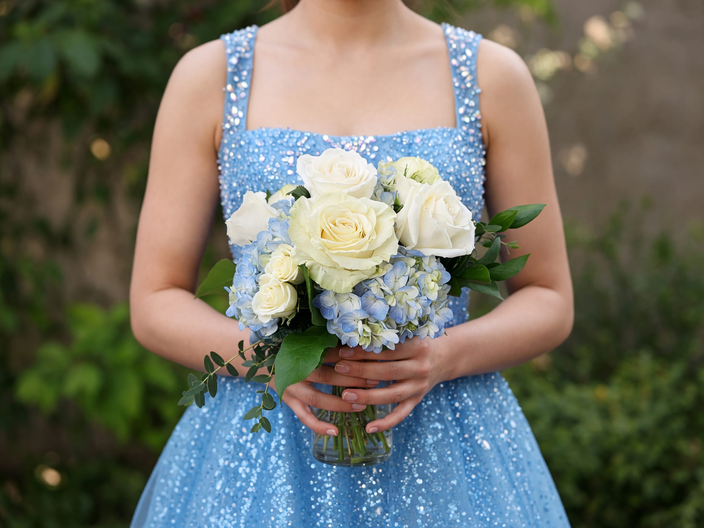 Woman in a blue dress holding a bouquet of white roses and blue hydrangeas in a glass vase