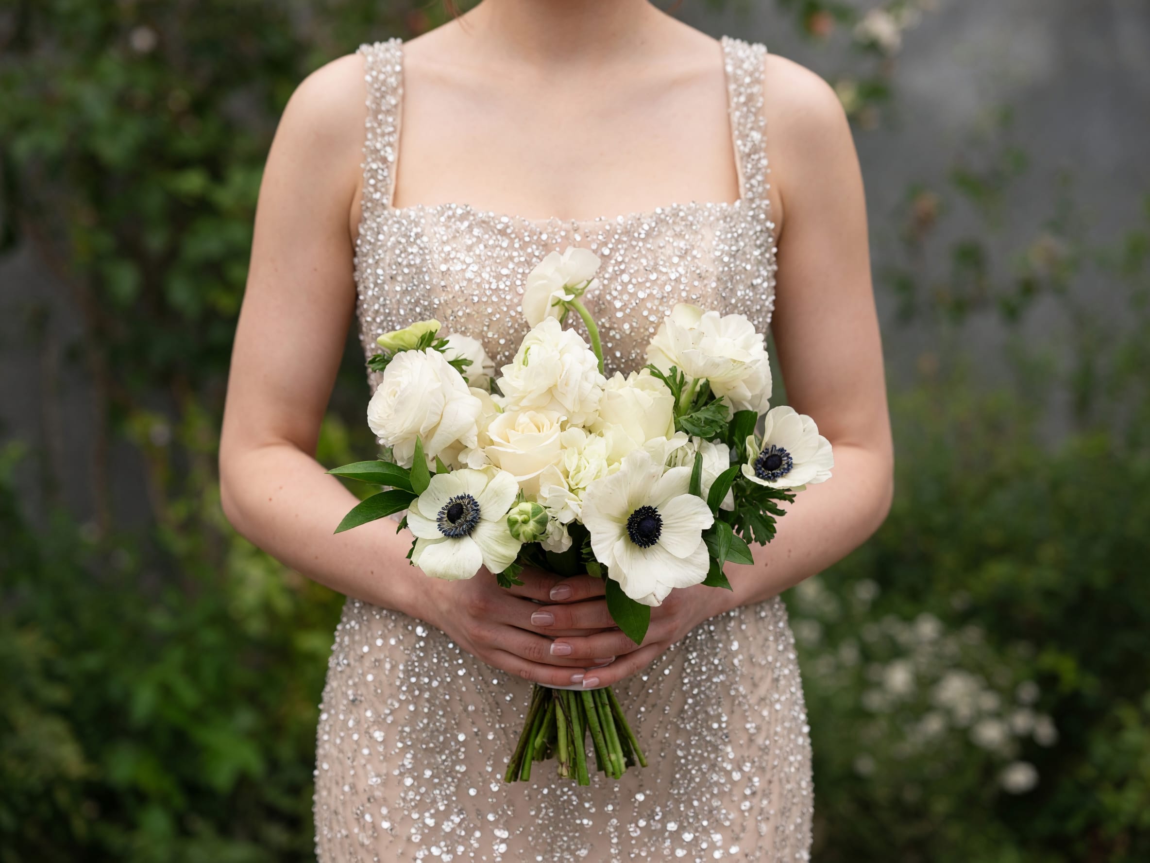Woman holding a white bridal bouquet with dark-centered anemones