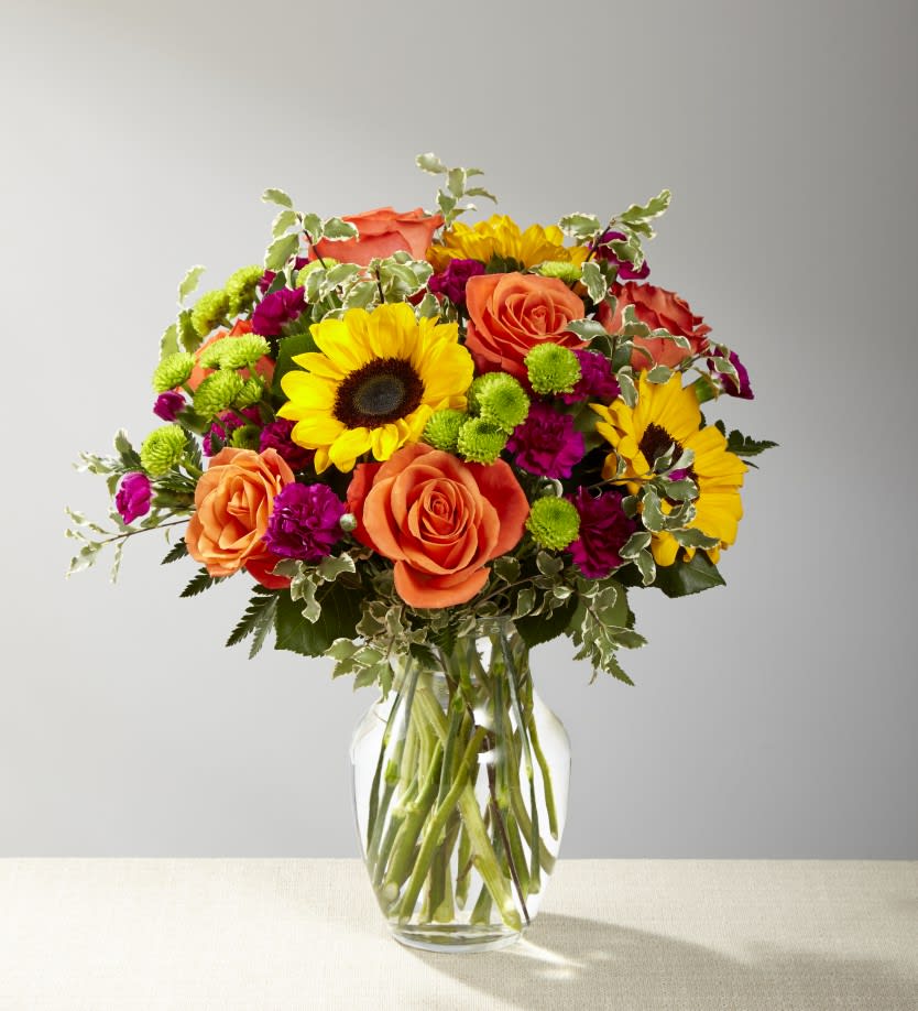 Color Crazy Bouquet - The Color Crazy Bouquet is a blend of orange roses, sunflowers, violet mini carnations, green button poms, and lush accent greens to create an incredible gift.   Ideal for birthdays, celebrations, or just because, this arrangement brings a burst of joy to any room.  Approximately 16"H x 14" W.  