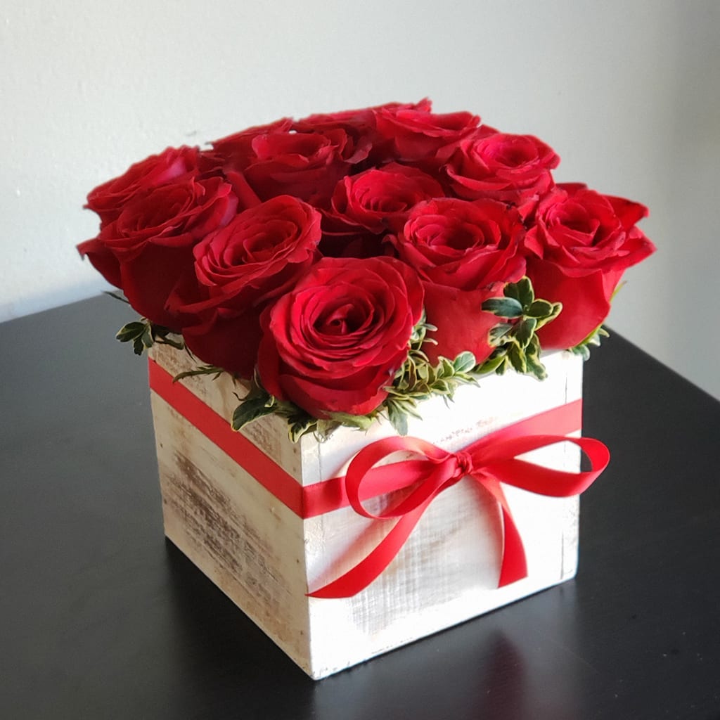 Red roses arranged in a white wooden box with a red ribbon