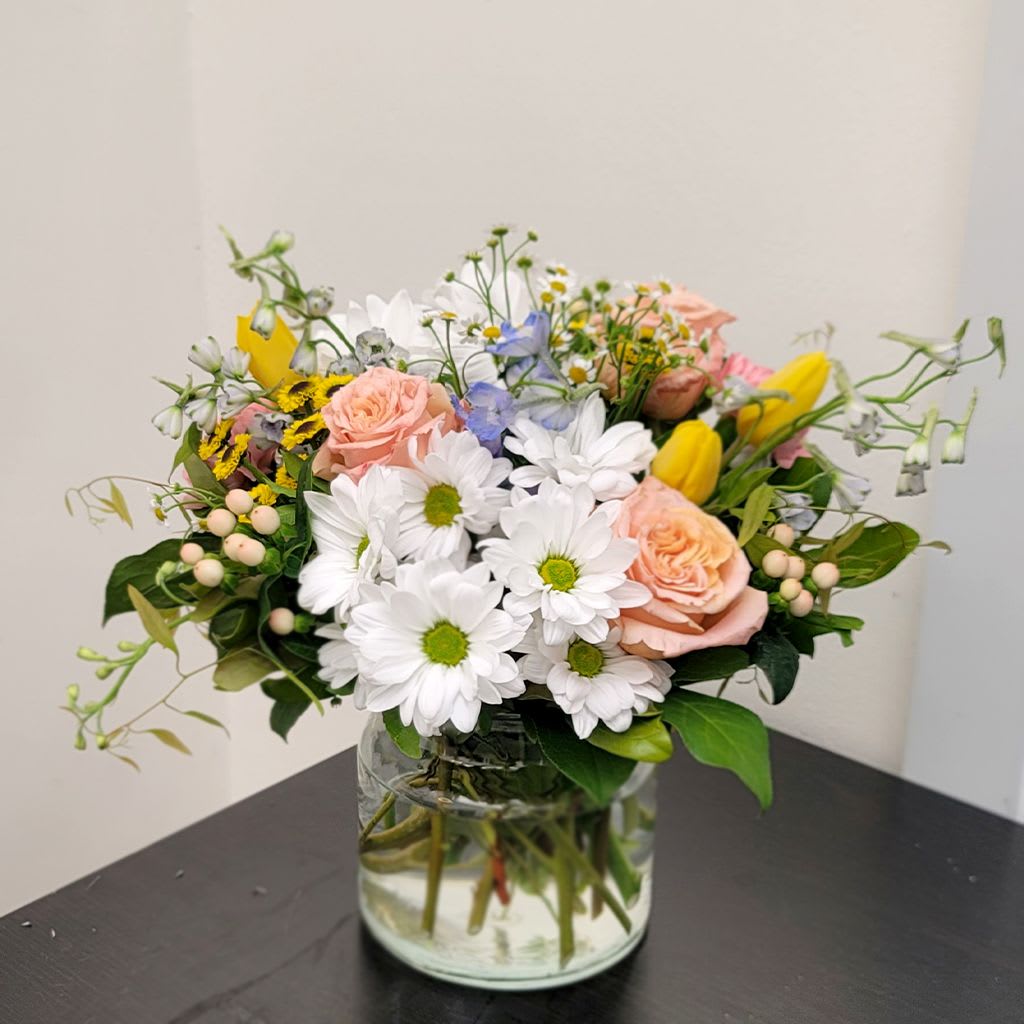 Sun Salutation Bouquet - Bright and uplifting, this refreshing bouquet features vibrant yellow tulips, cheerful white daisies, soft pink roses, and a variety of wildflowers capturing the warmth of a perfect sunny day.   Designed to bring a sense of calm and a breath of fresh spring air, it’s the perfect gift for any occasion.  Approximate Size: 13" H x 17" W. Order now to brighten someone's day!