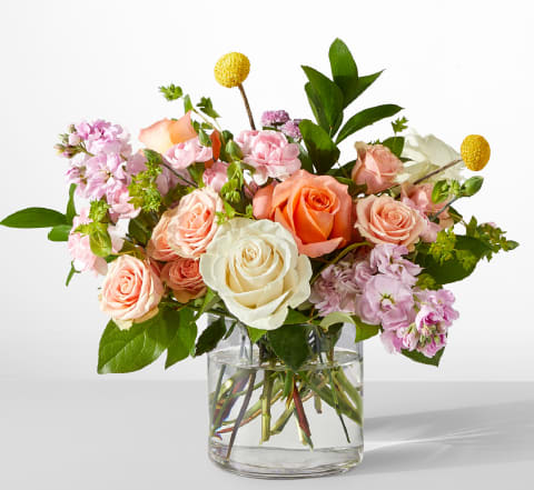 Bouquet of peach, white, and pink roses in a clear glass vase