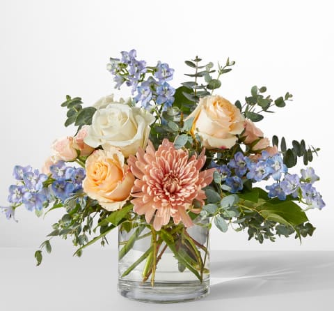 Mixed bouquet of roses, chrysanthemum, and blue flowers in a glass vase