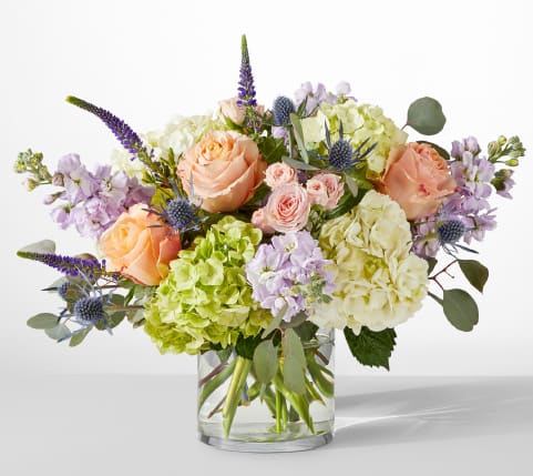 Bouquet of peach roses, hydrangeas, and lavender flowers in a glass vase