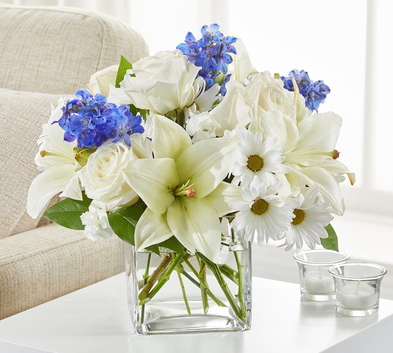 White lilies, roses, and daisies with blue flowers in a glass vase