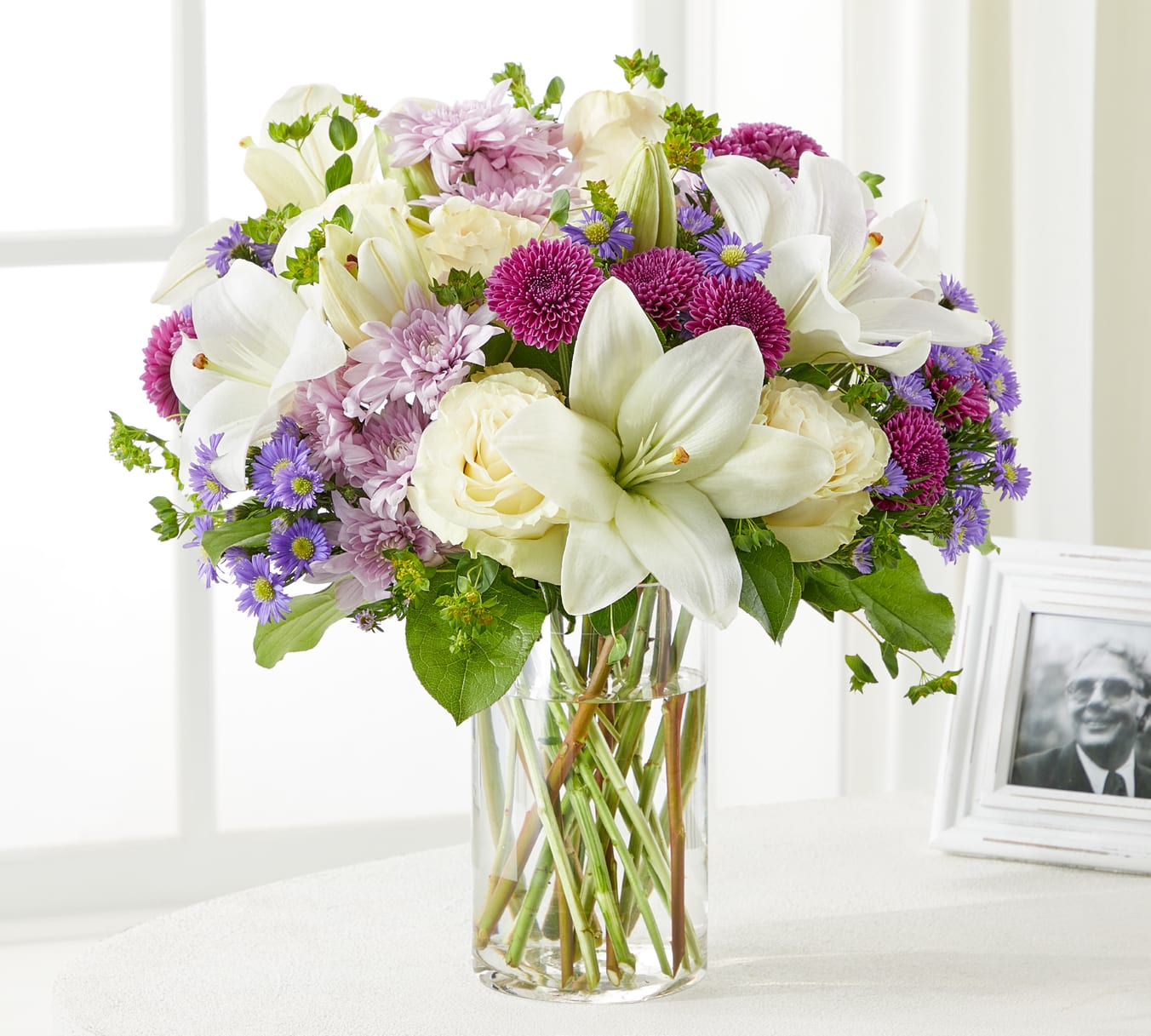 Bouquet of white lilies, cream roses, and purple flowers in a glass vase