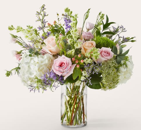 Pastel bouquet of roses, hydrangeas, and purple flowers in a clear glass vase