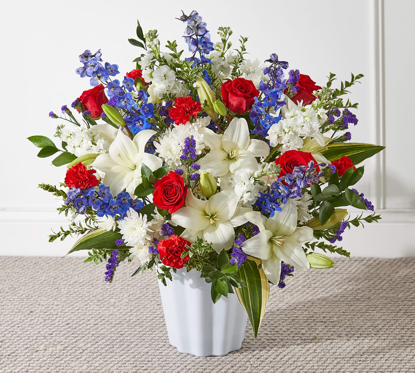 Mixed bouquet of red roses, white lilies, and blue flowers in a white vase