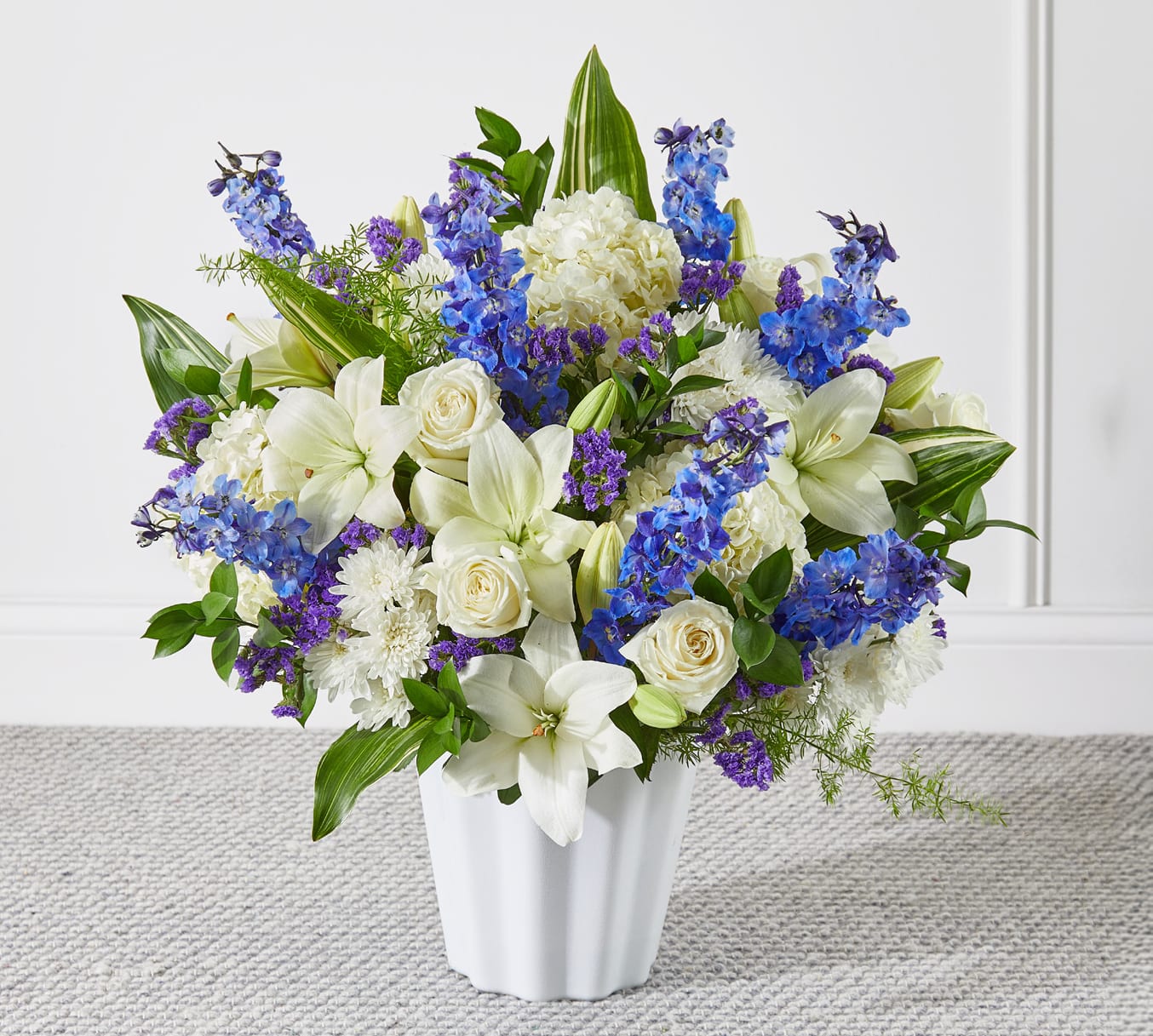 White lilies, roses, and blue-purple flowers in a white vase