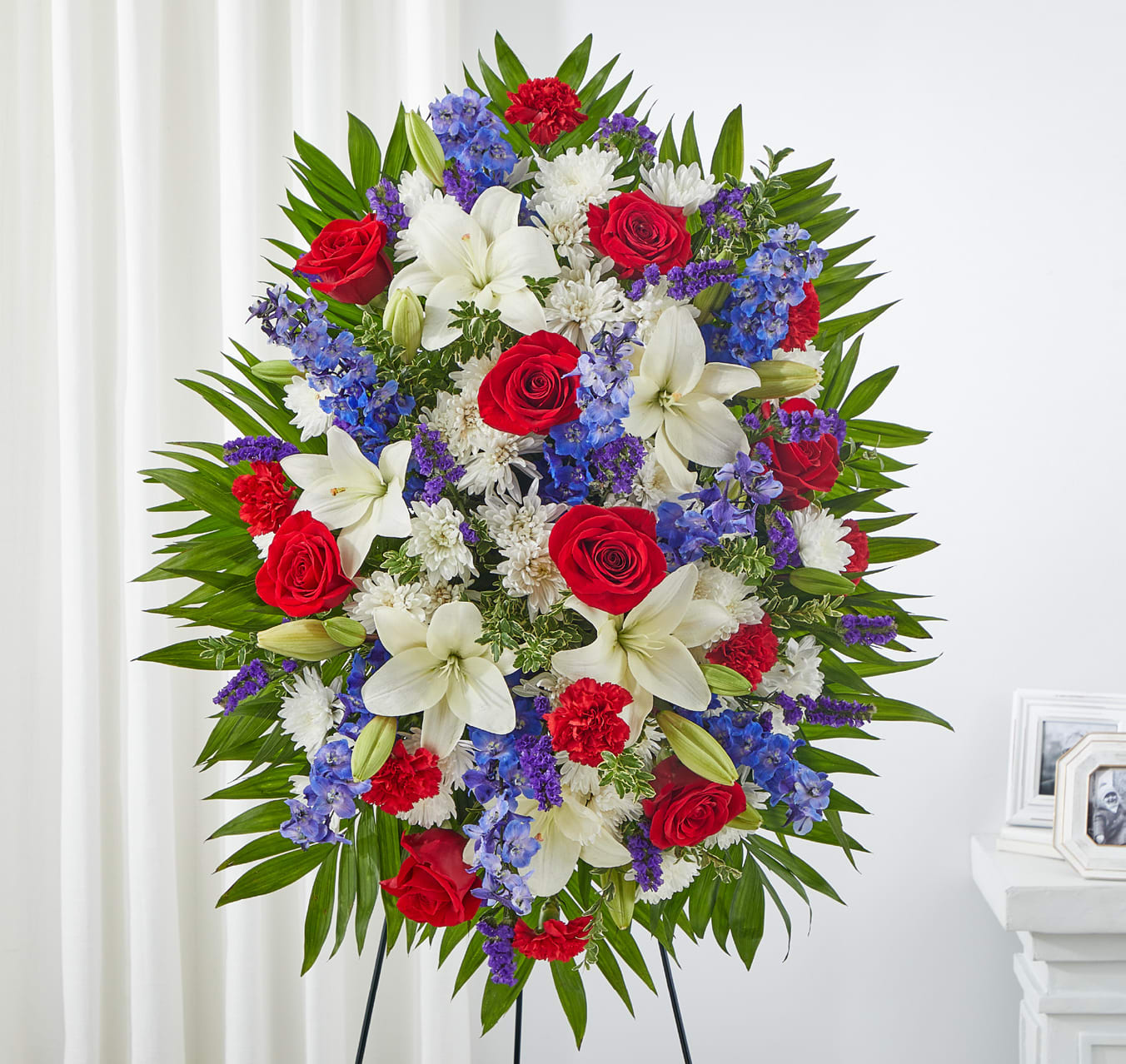 Large standing floral spray with red roses, white lilies, and blue flowers