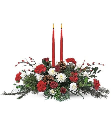 Low Christmas centerpiece with red and white flowers, evergreens, pinecones, and two red taper candles.