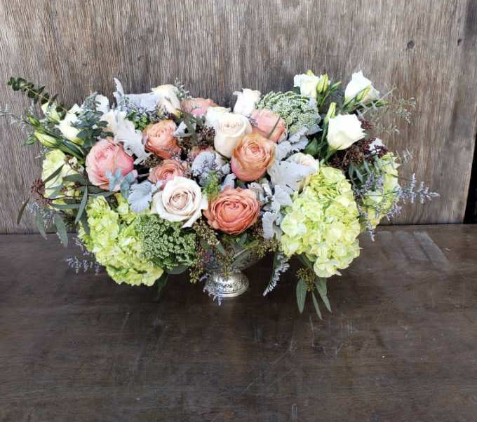 Low floral centerpiece with peach and white roses and pale green hydrangeas in a silver vase
