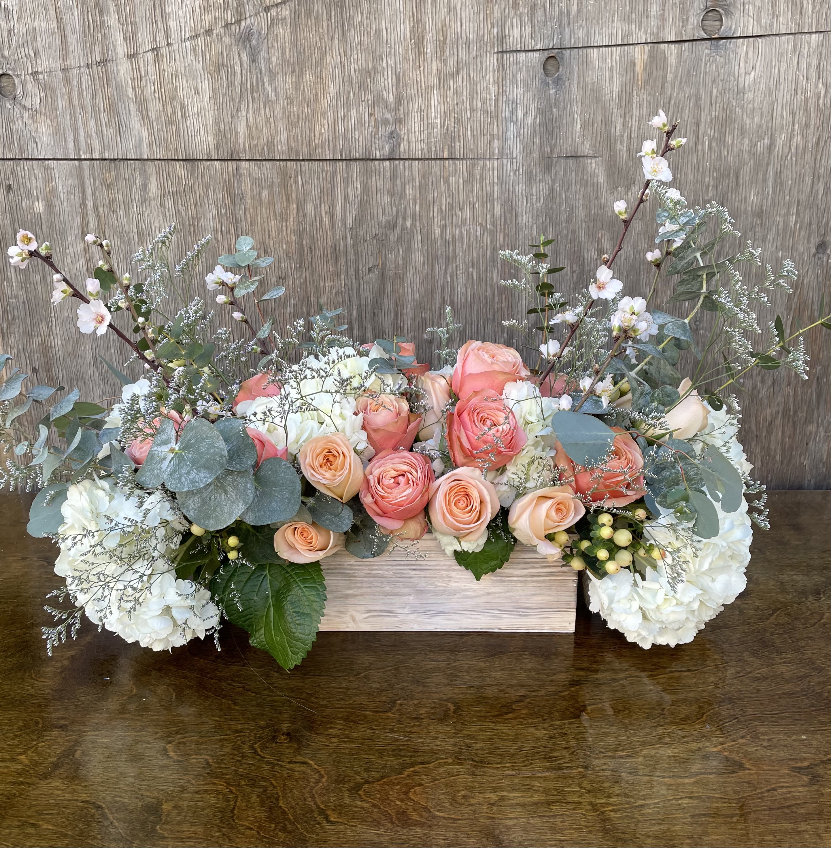 Low floral arrangement of peach and white roses with white hydrangeas in a wooden box