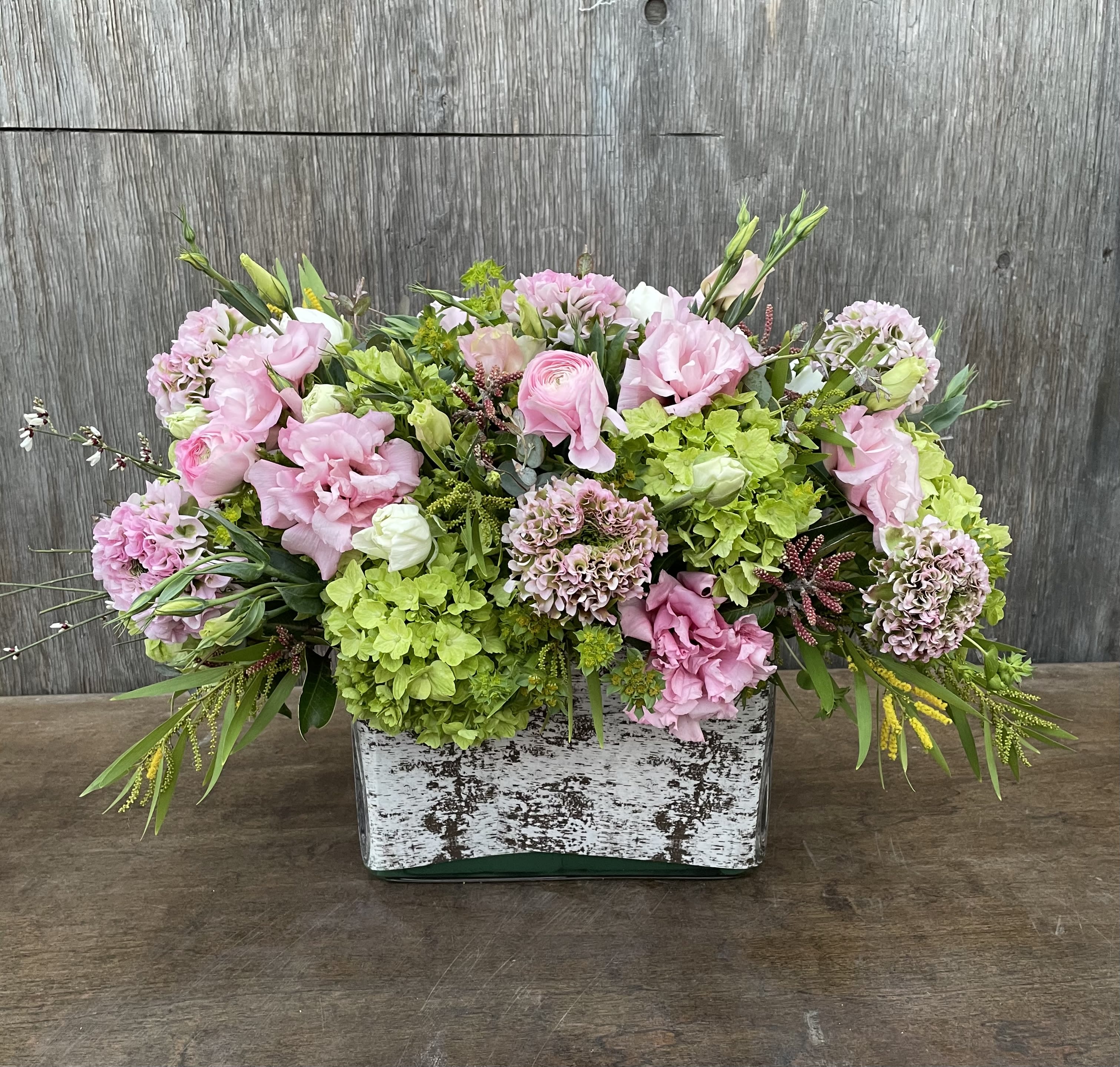 Pink and green floral arrangement in a rustic rectangular container