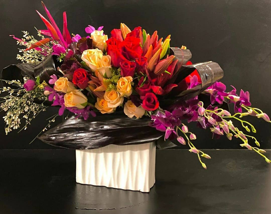 Large bouquet of red, peach, and purple flowers in black wrap