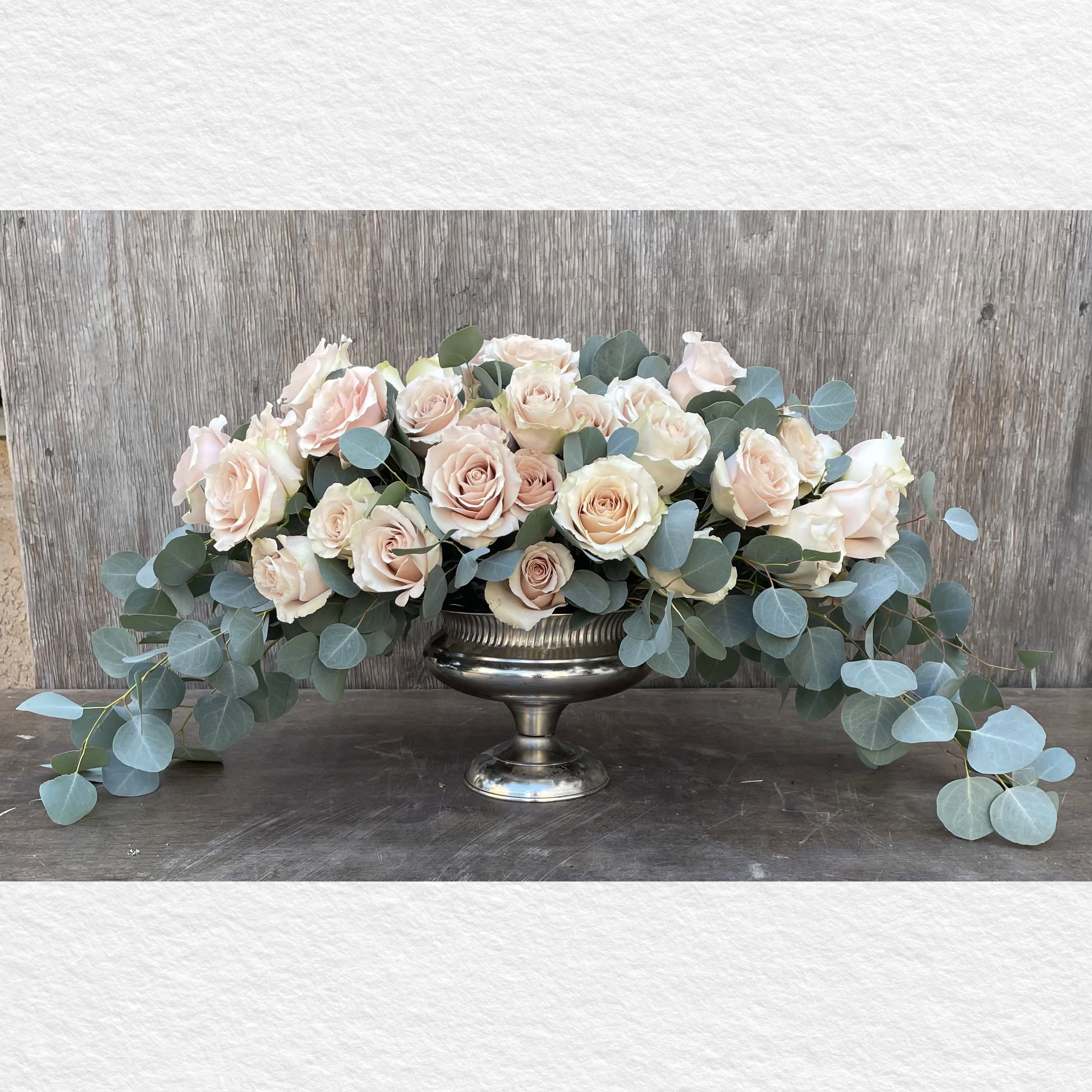 Blush roses arranged in a silver pedestal bowl with trailing eucalyptus