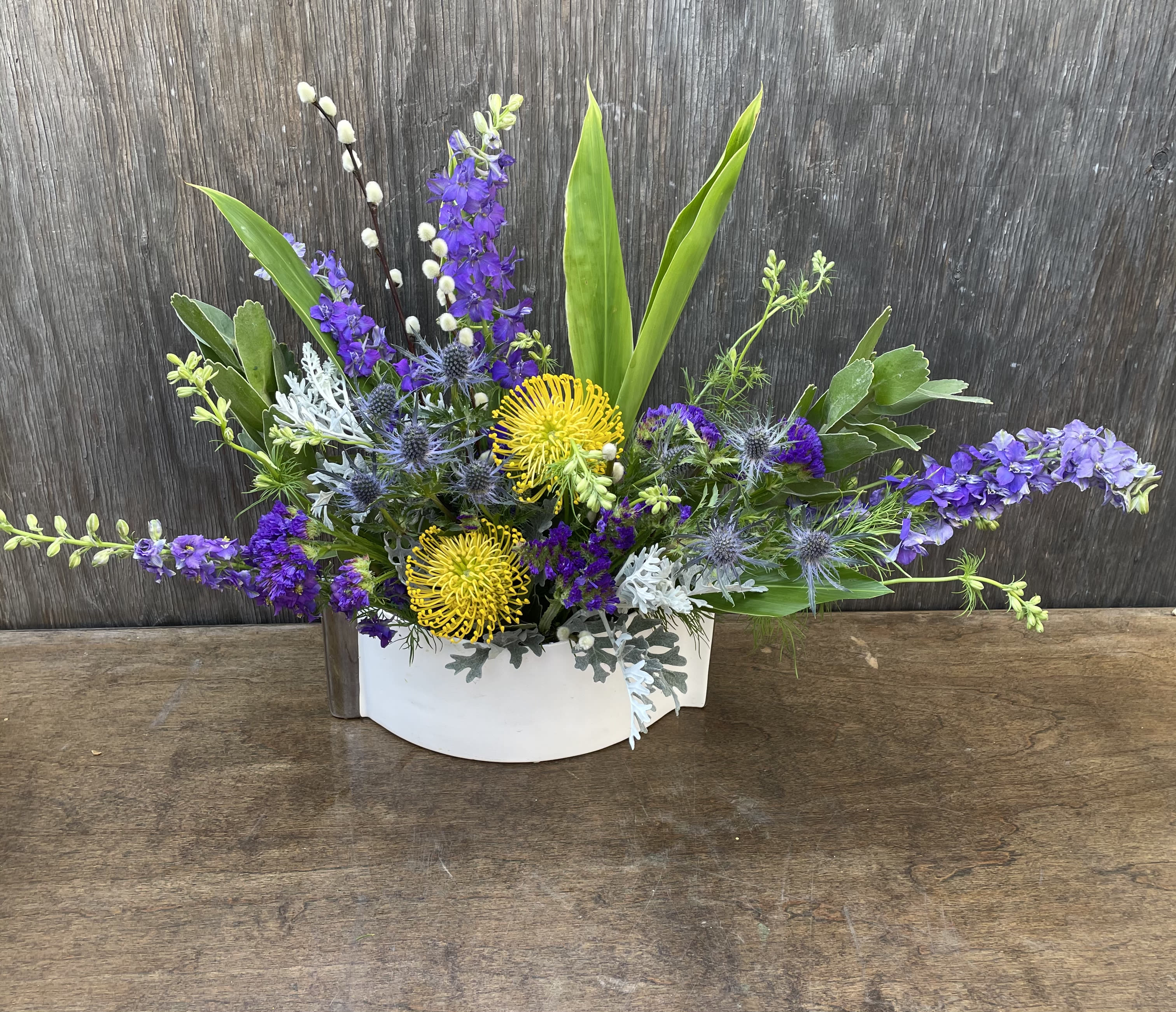 Low floral arrangement with purple and yellow blooms in a white container