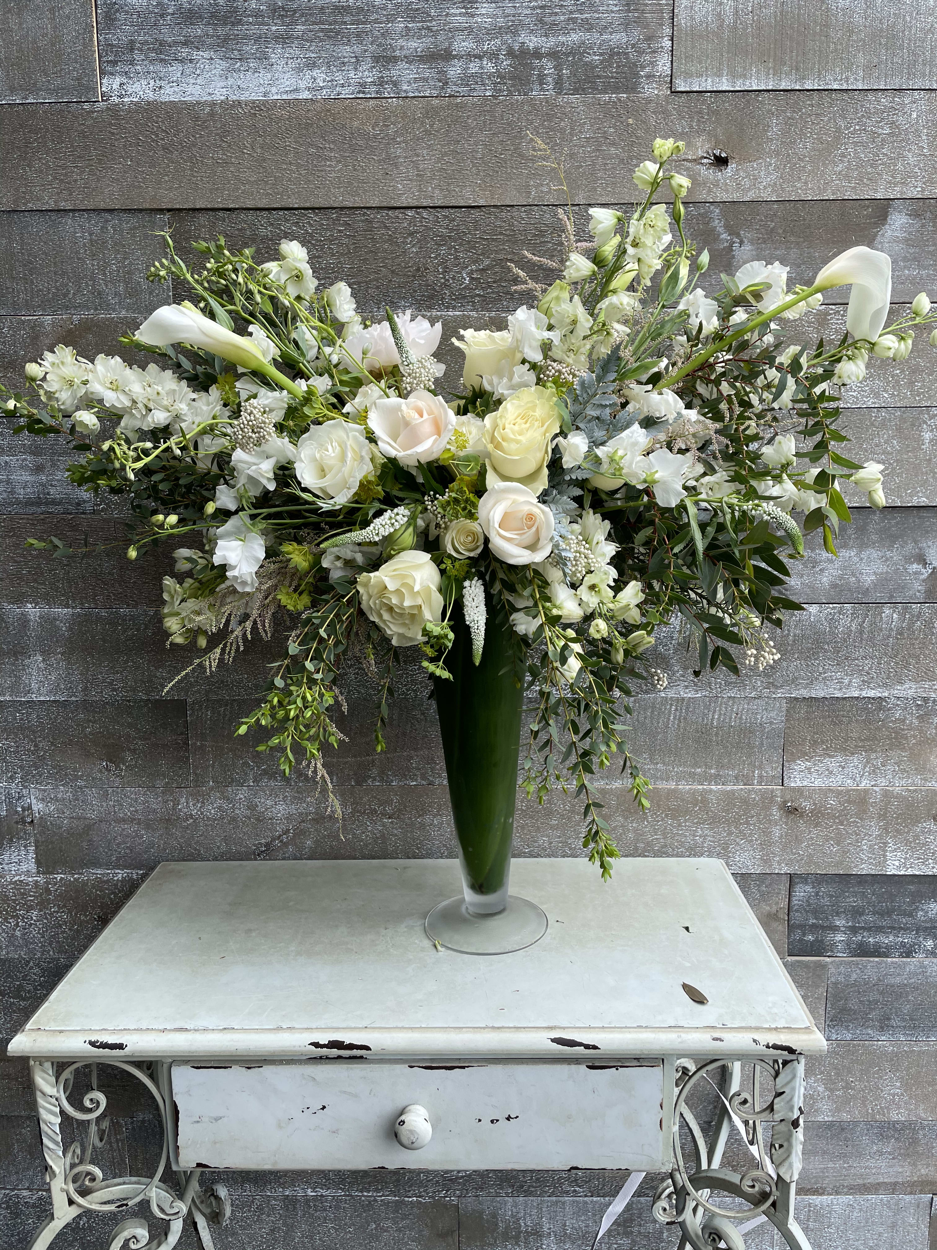 White floral arrangement in a tall green vase with cascading stems