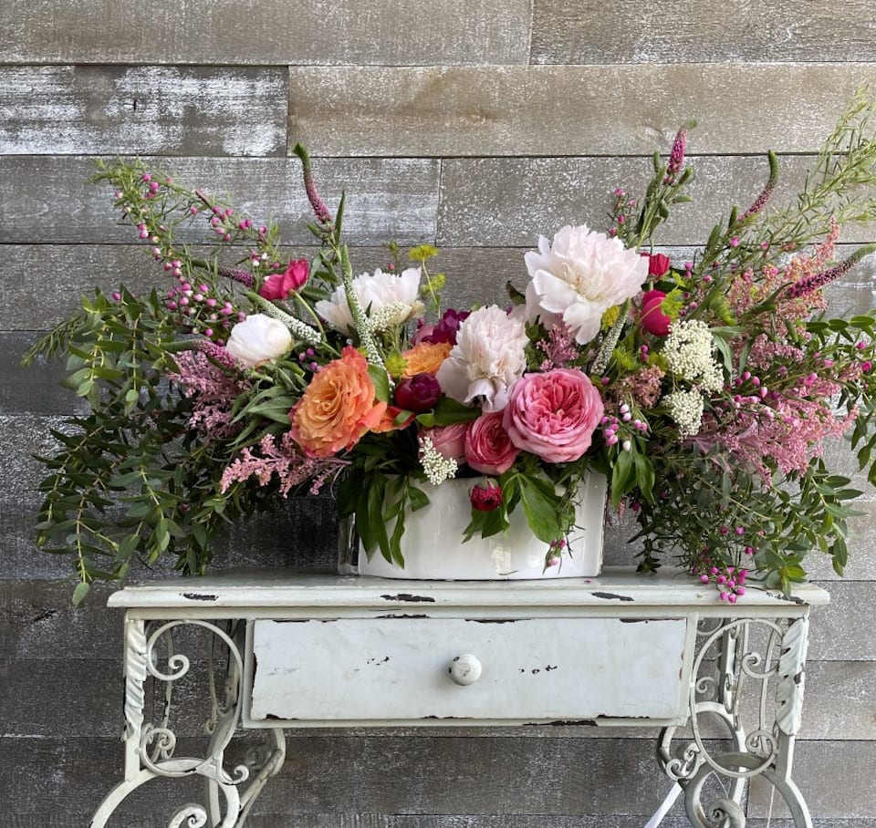 Large mixed floral arrangement in a white container on a small table