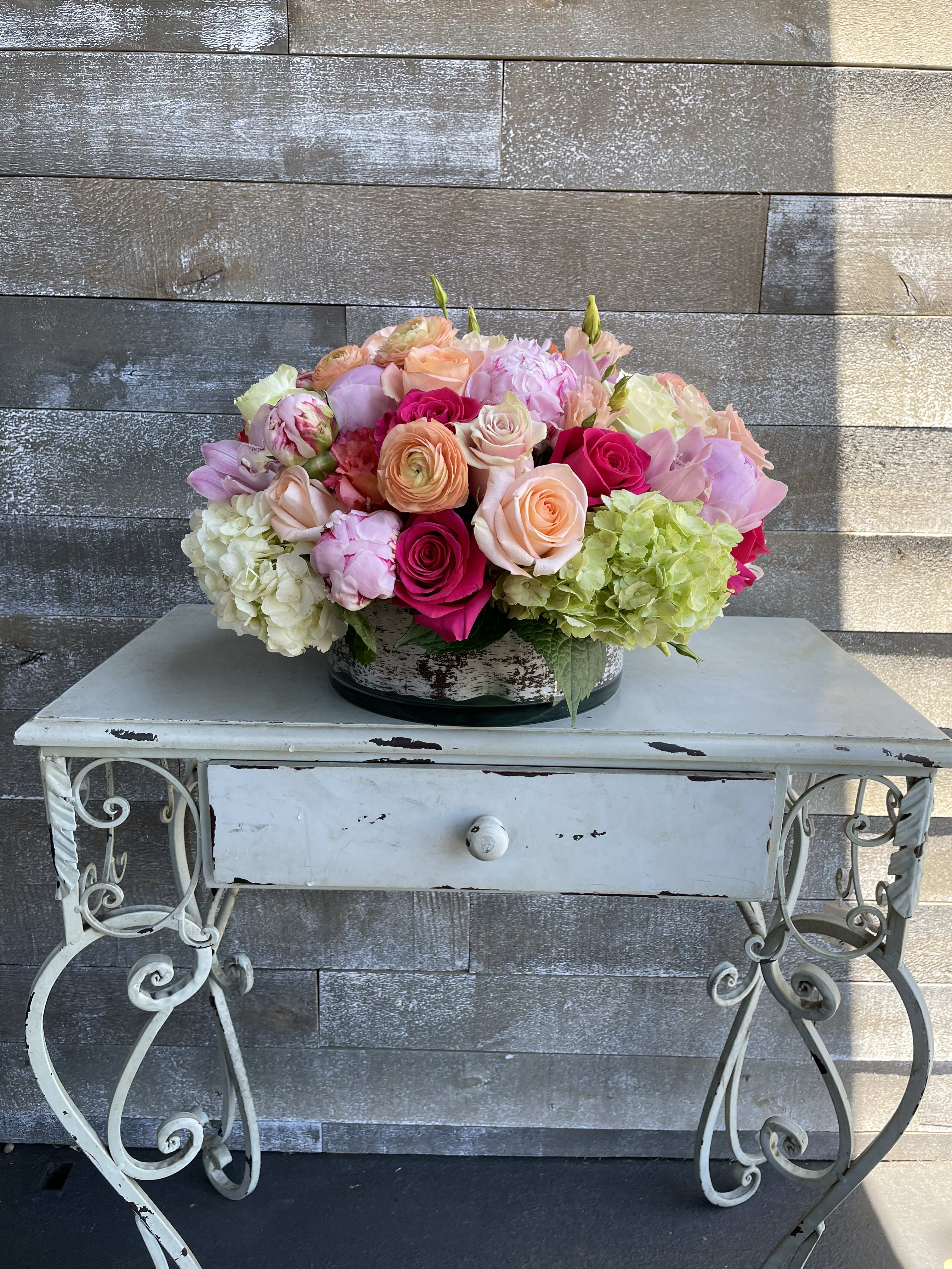 Mixed bouquet of pink, peach, and green flowers in a low container