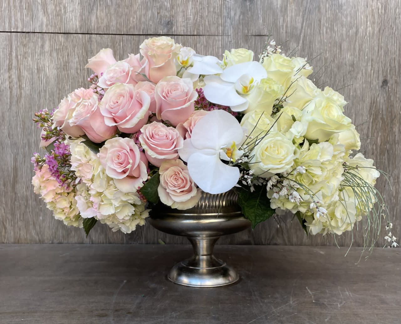 Pink and white roses with orchids in a silver pedestal vase