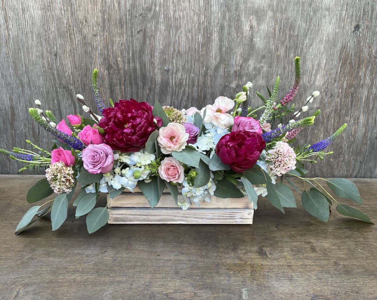Low floral arrangement with pink and burgundy blooms in a wooden box